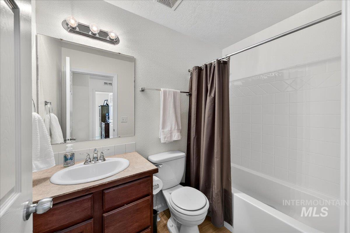 Bathroom featuring a textured wall, shower / bath combination with curtain, vanity, and a textured ceiling