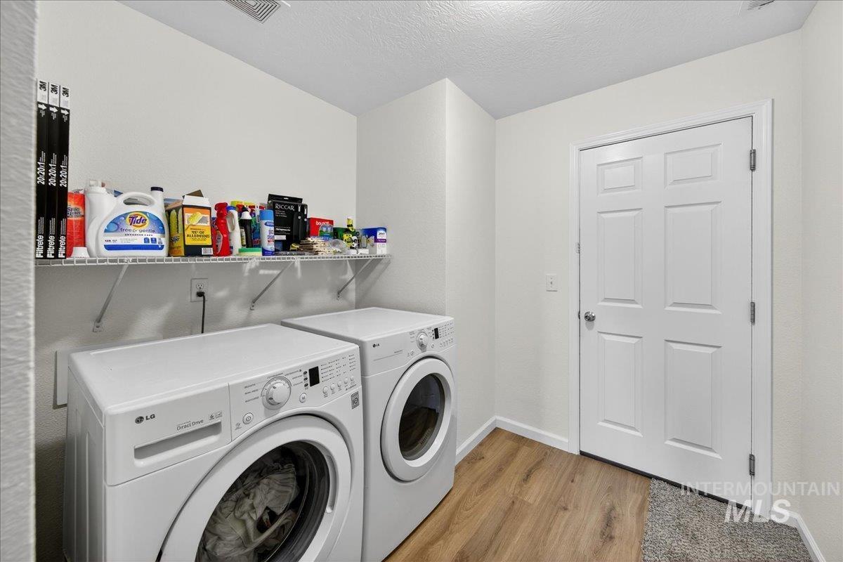 Washroom with light wood-type flooring, washing machine and clothes dryer, and a textured ceiling