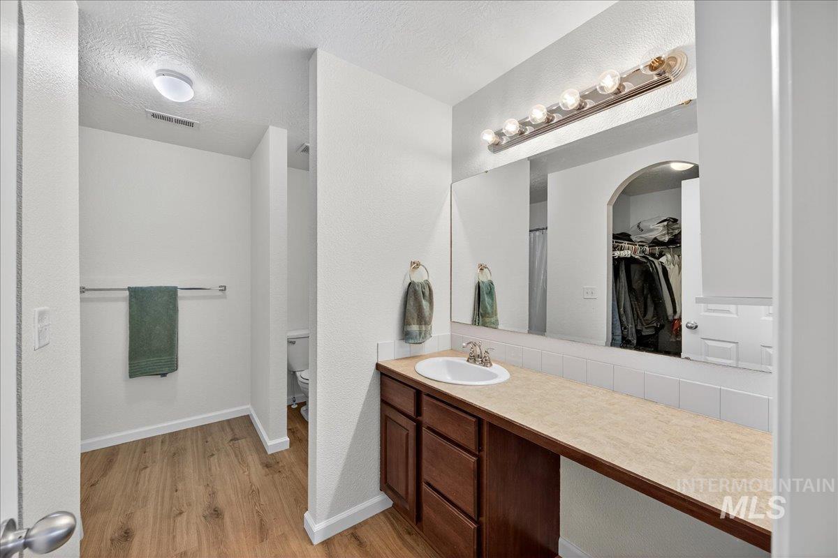 Bathroom with vanity, light wood-style flooring, a spacious closet, a textured ceiling, and a textured wall
