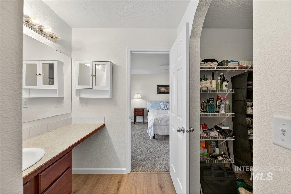 Full bath featuring vanity, light wood-style floors, a textured wall, and ensuite bath
