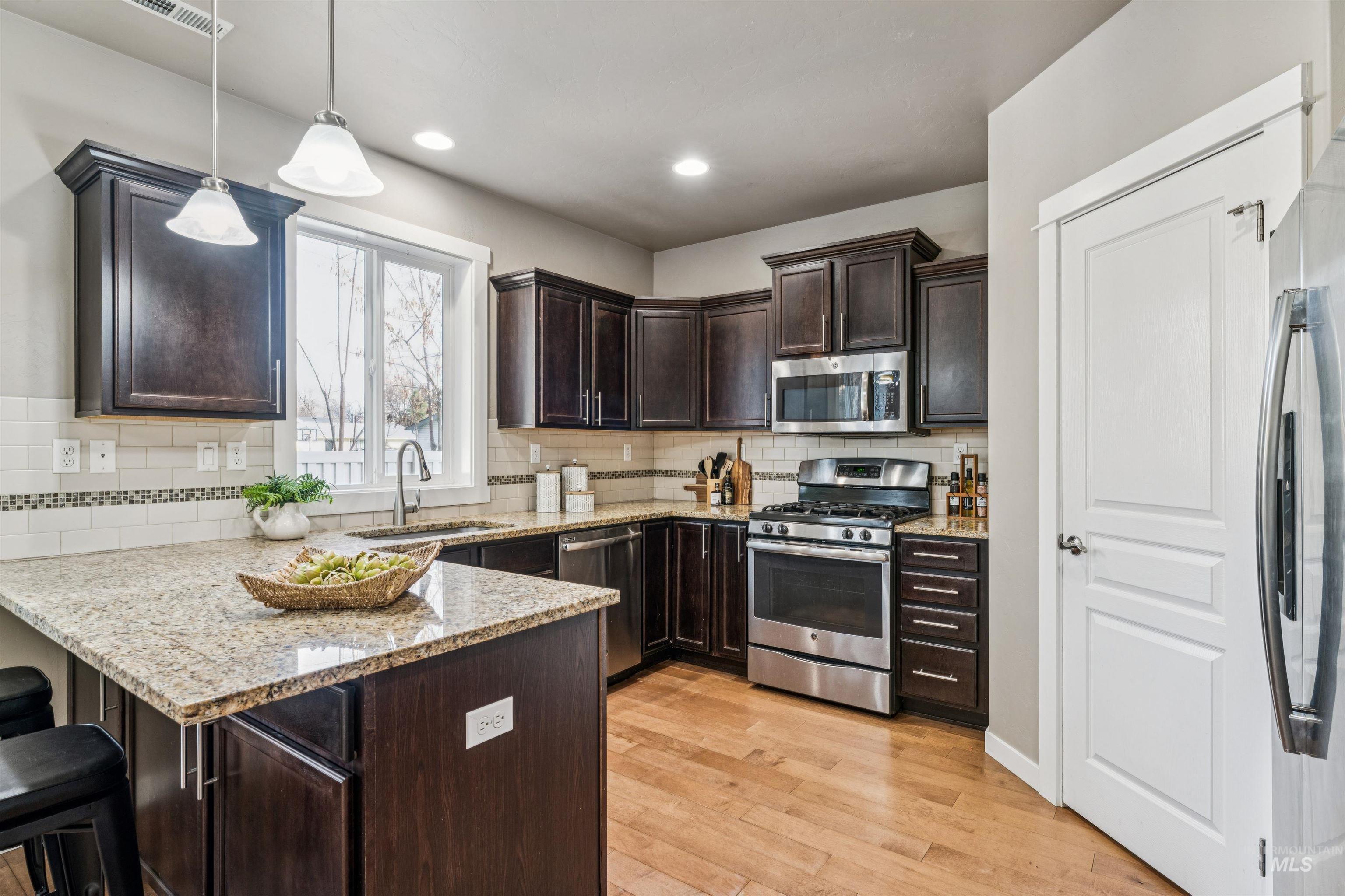 Kitchen featuring dark brown cabinets, appliances with stainless steel finishes, a kitchen breakfast bar, light stone countertops, and recessed lighting