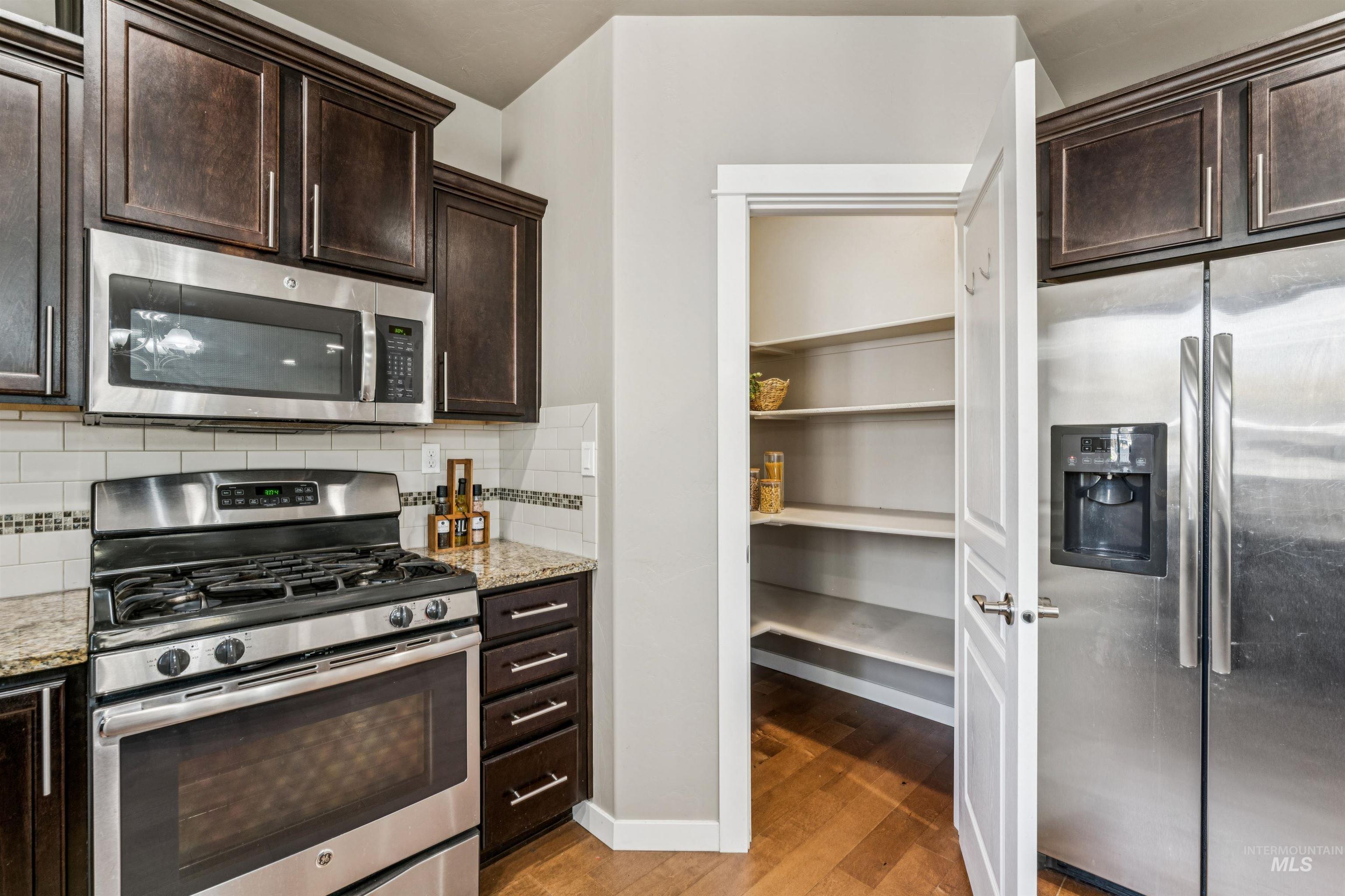 Kitchen featuring stainless steel appliances, dark brown cabinets, light wood-style flooring, backsplash, and light stone countertops