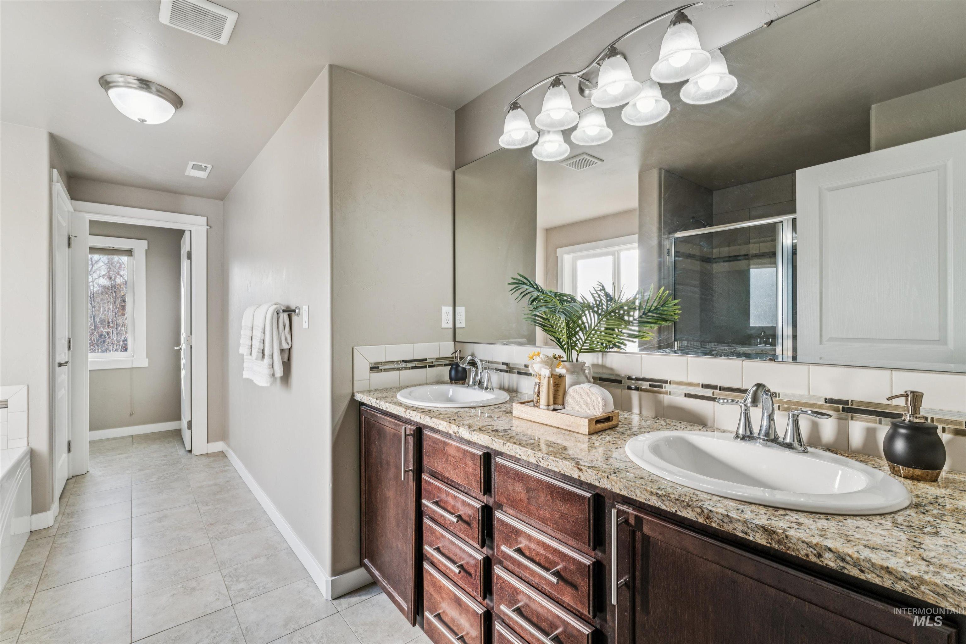 Full bath with a stall shower, double vanity, tasteful backsplash, and light tile patterned floors