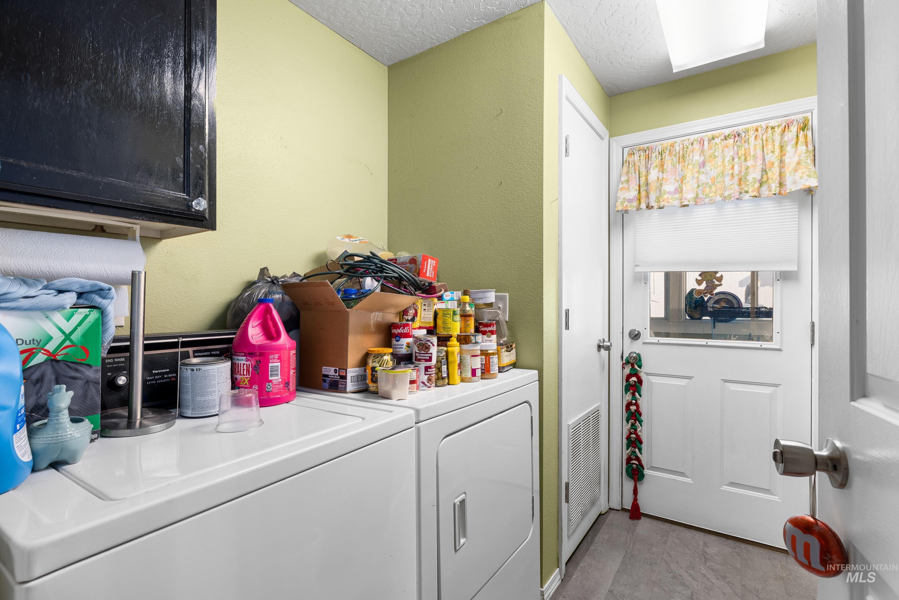 Laundry area with cabinet space, independent washer and dryer, a textured ceiling, and a textured wall