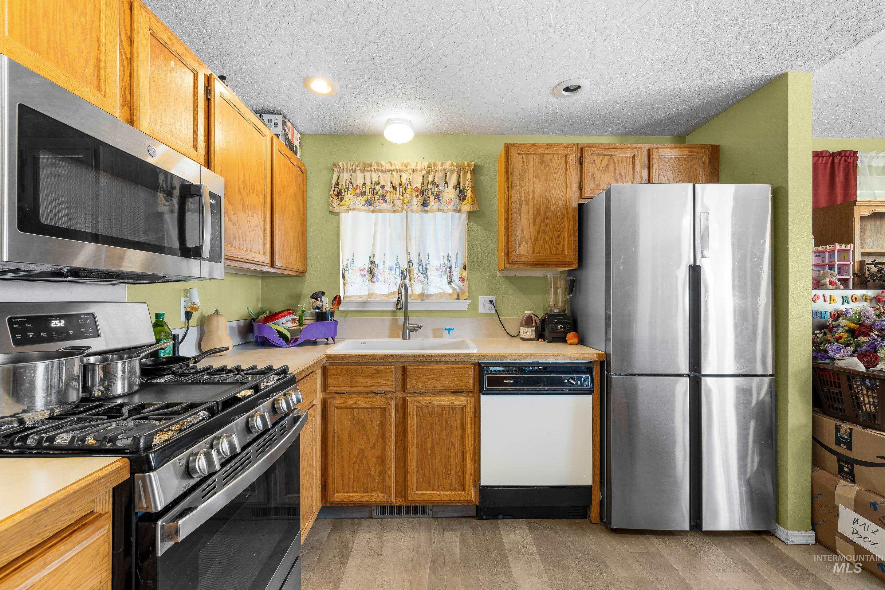 Kitchen with stainless steel appliances, a textured ceiling, light countertops, light wood-style flooring, and brown cabinets