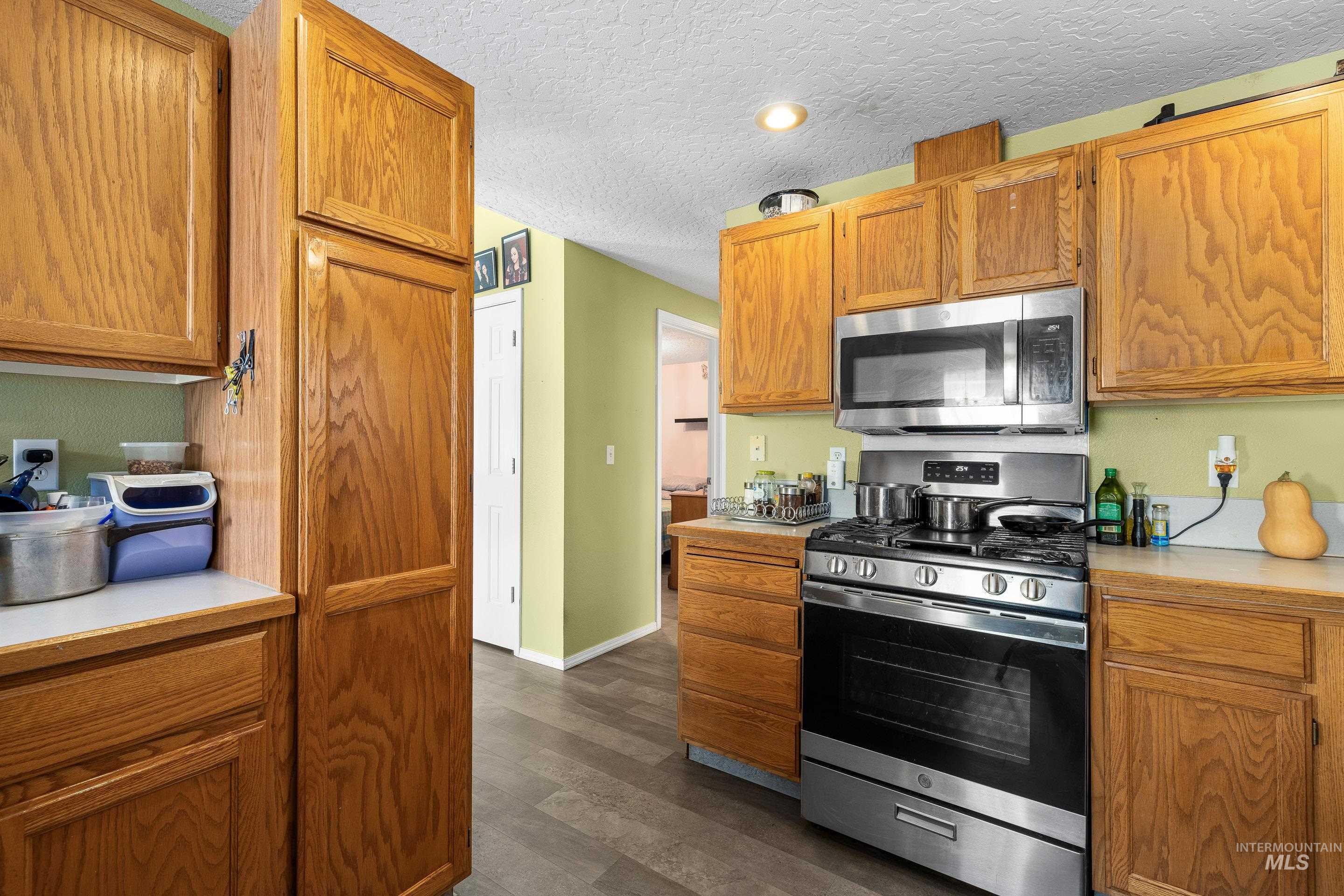 Kitchen with stainless steel appliances, light countertops, dark wood-style flooring, a textured ceiling, and brown cabinetry