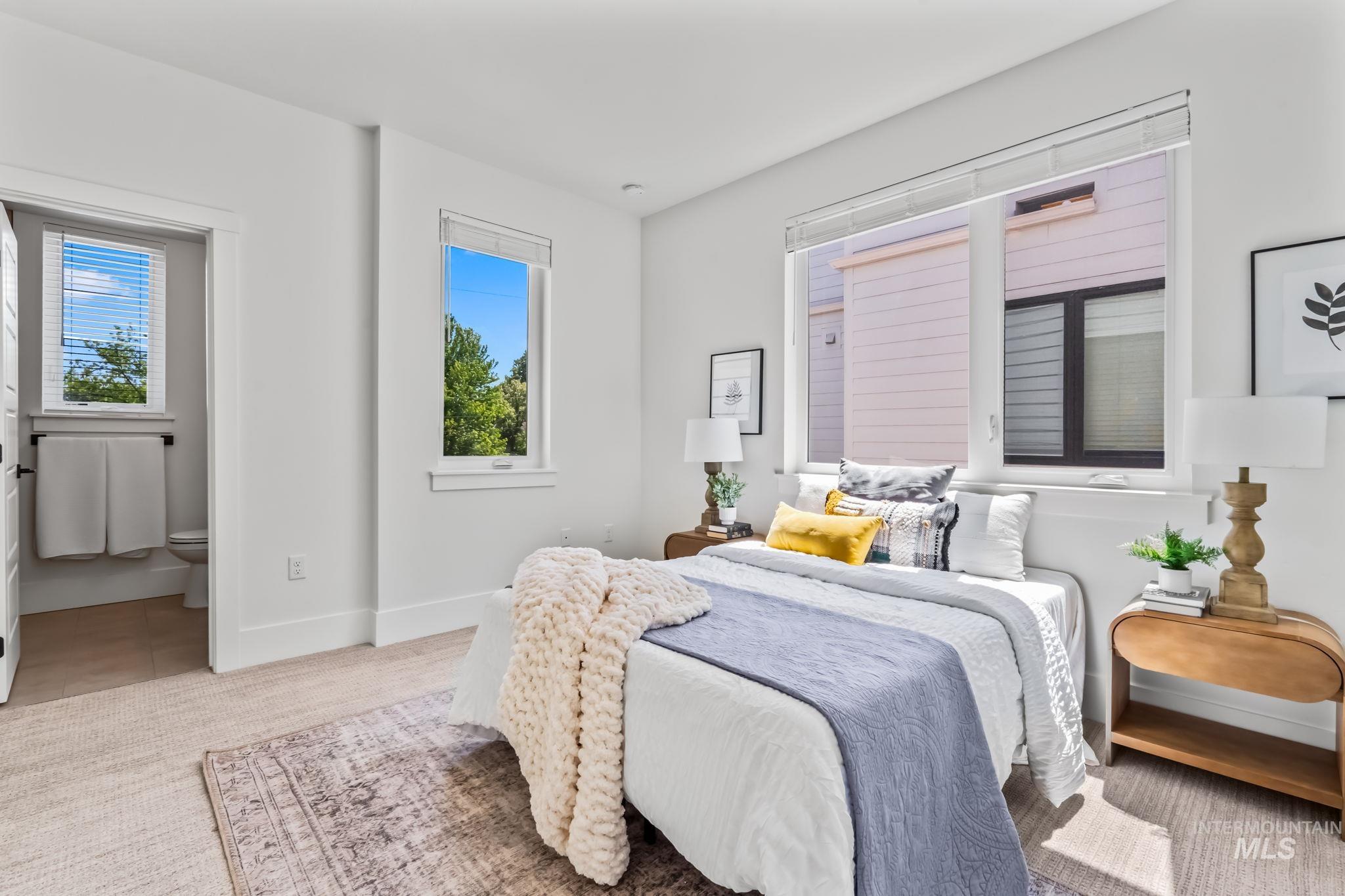 Carpeted bedroom with multiple windows, ensuite bath, and tile patterned flooring