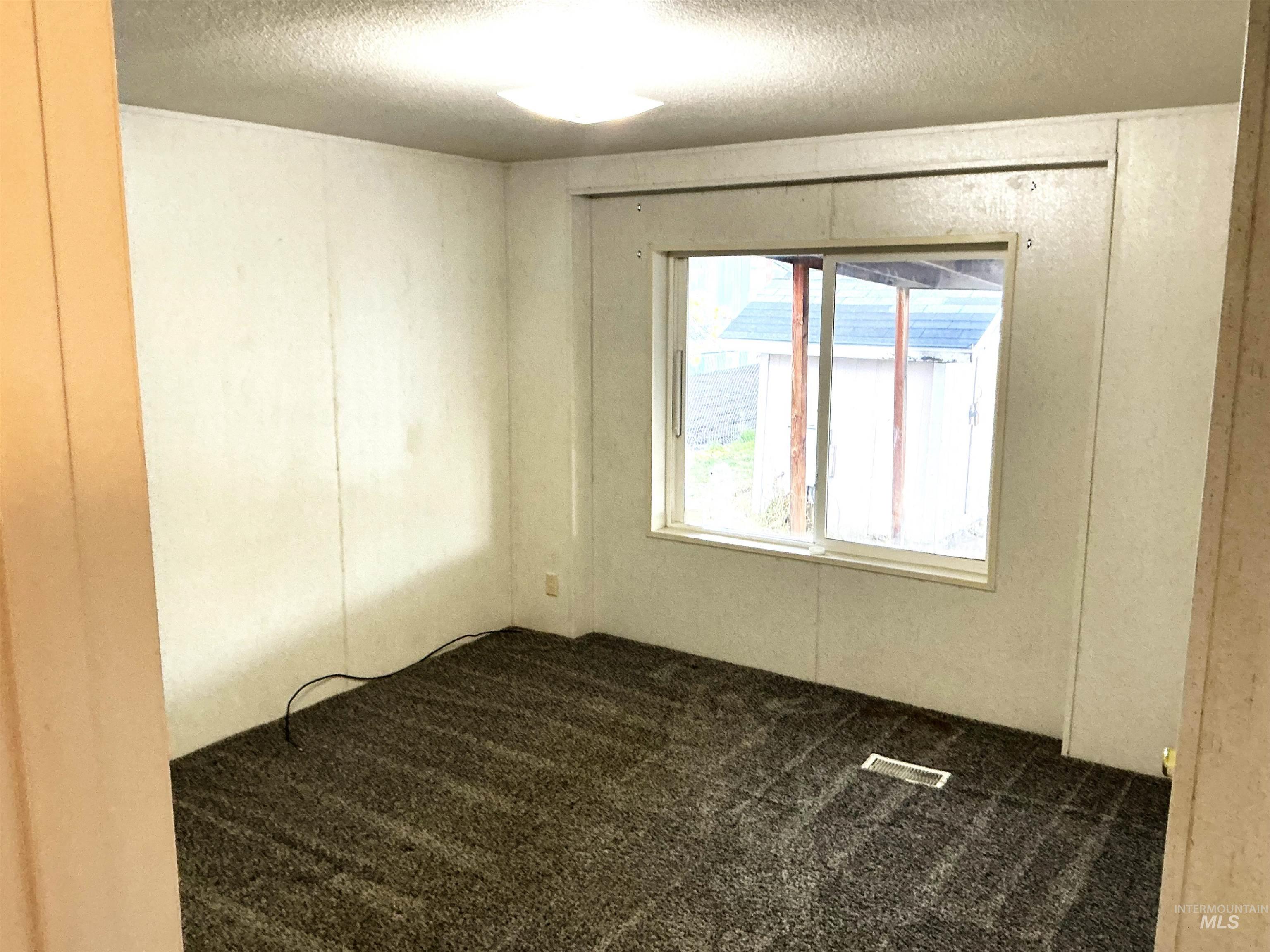 Empty room with dark carpet and a textured ceiling