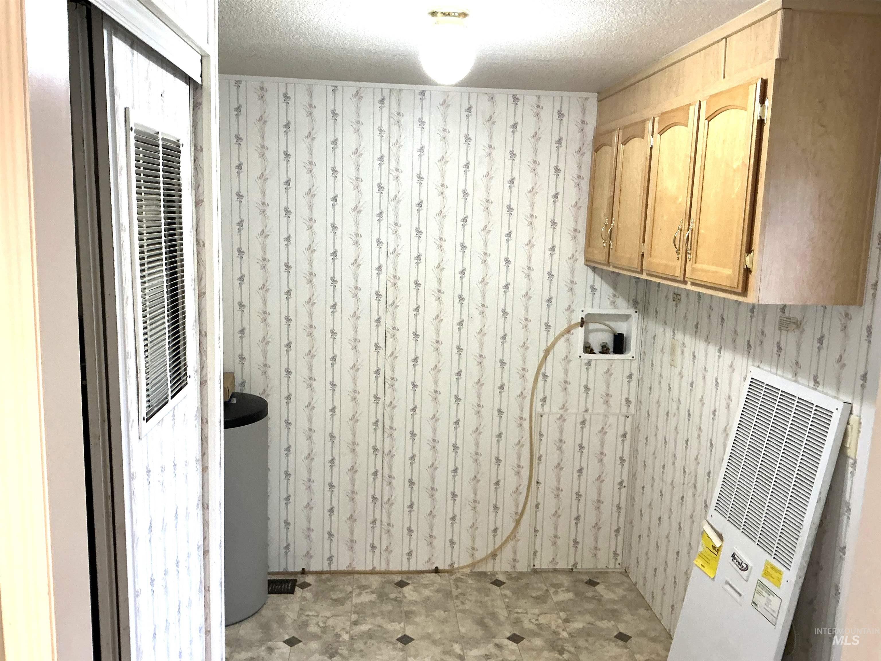 Washroom with a heating unit, a textured ceiling, hookup for a washing machine, wallpapered walls, and cabinet space