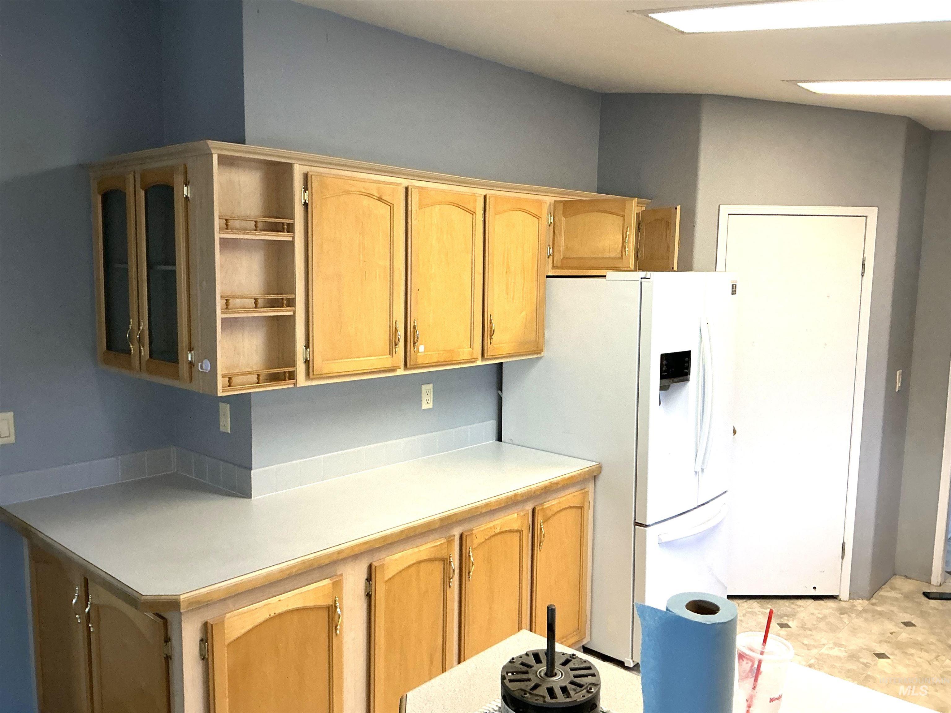 Kitchen featuring light countertops, white fridge with ice dispenser, and open shelves