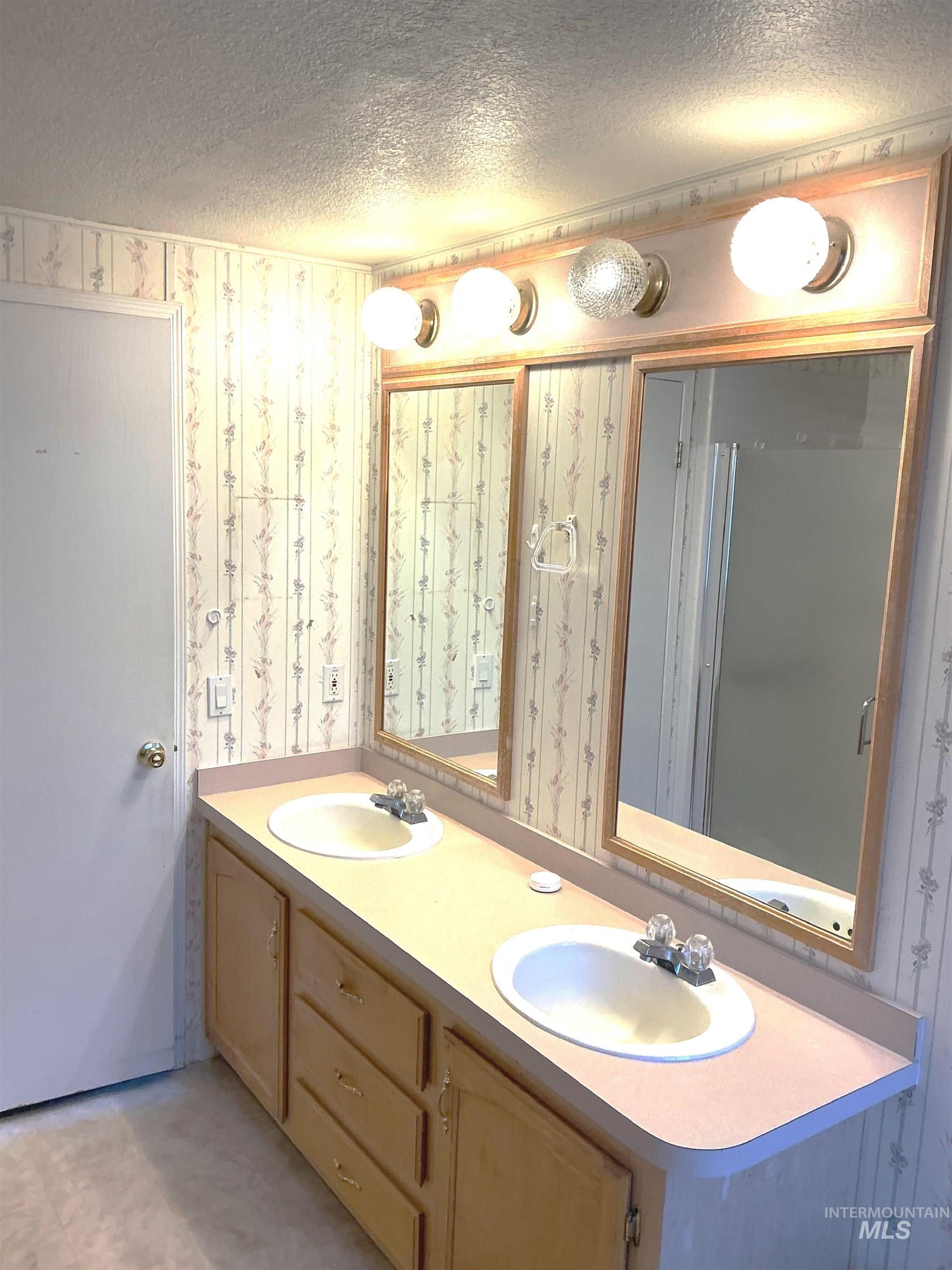 Full bathroom with wallpapered walls, double vanity, and a textured ceiling