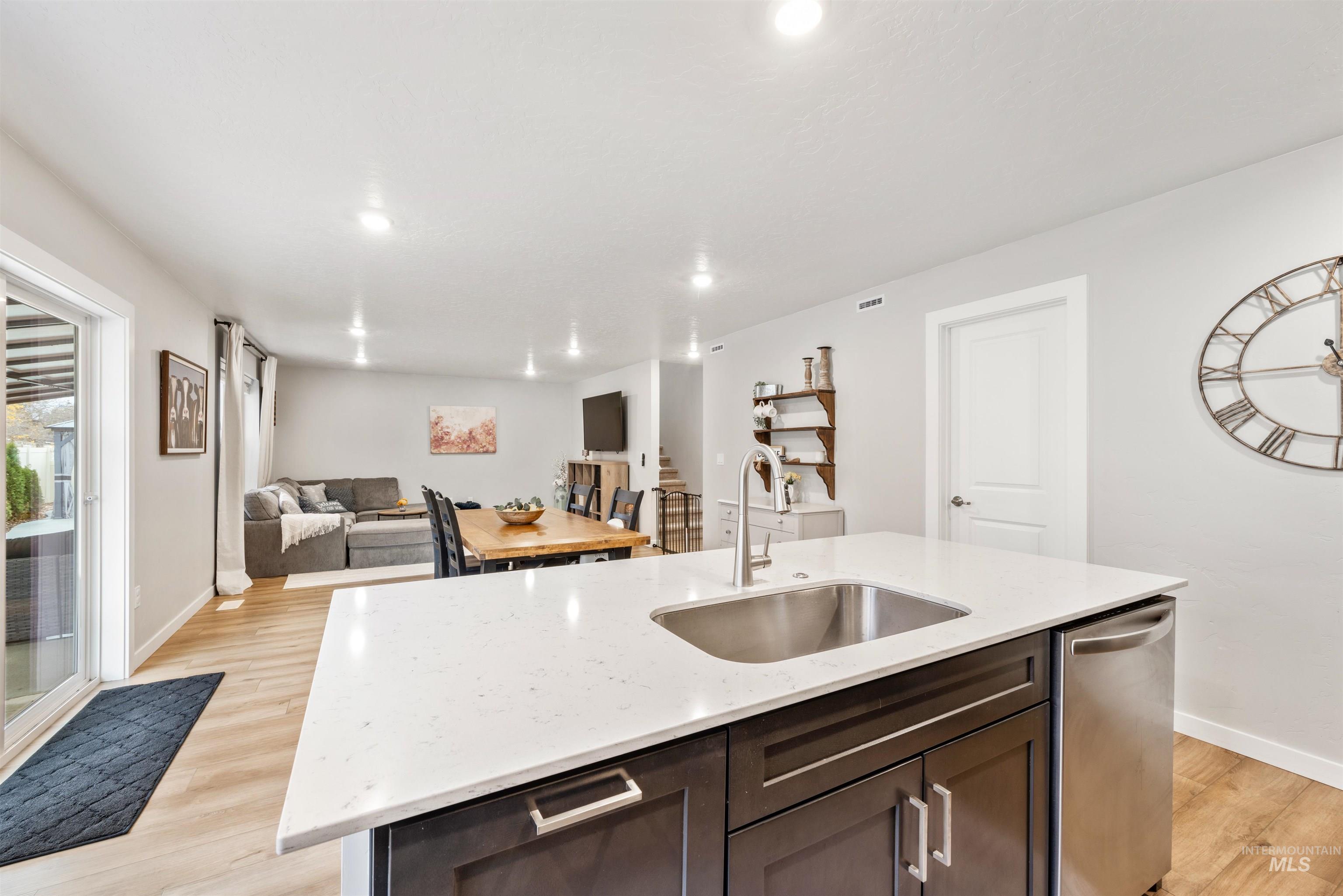 Kitchen with dark brown cabinets, open floor plan, a center island with sink, light wood finished floors, and light stone countertops