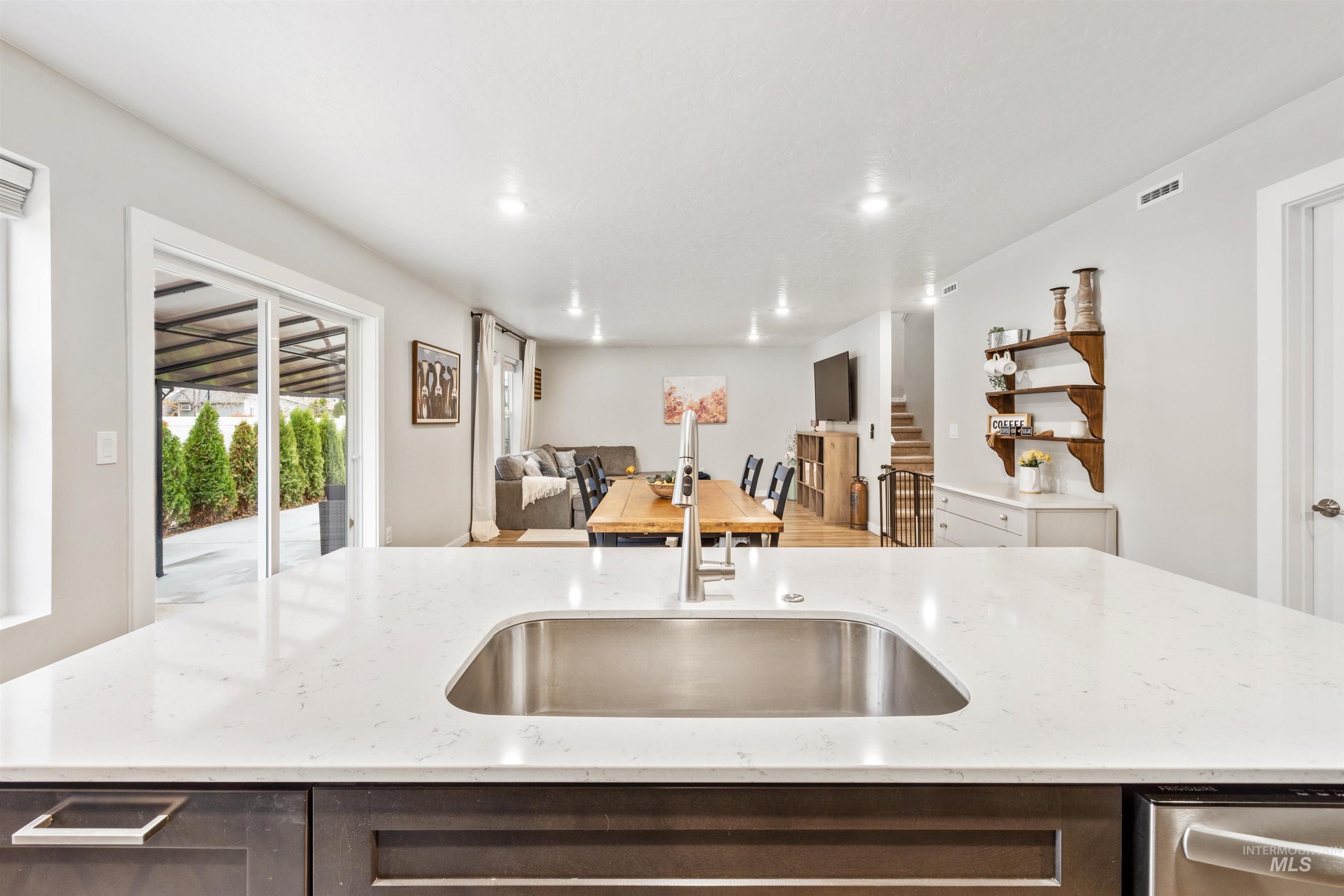 Kitchen featuring dark brown cabinets, a center island with sink, light stone countertops, open floor plan, and open shelves