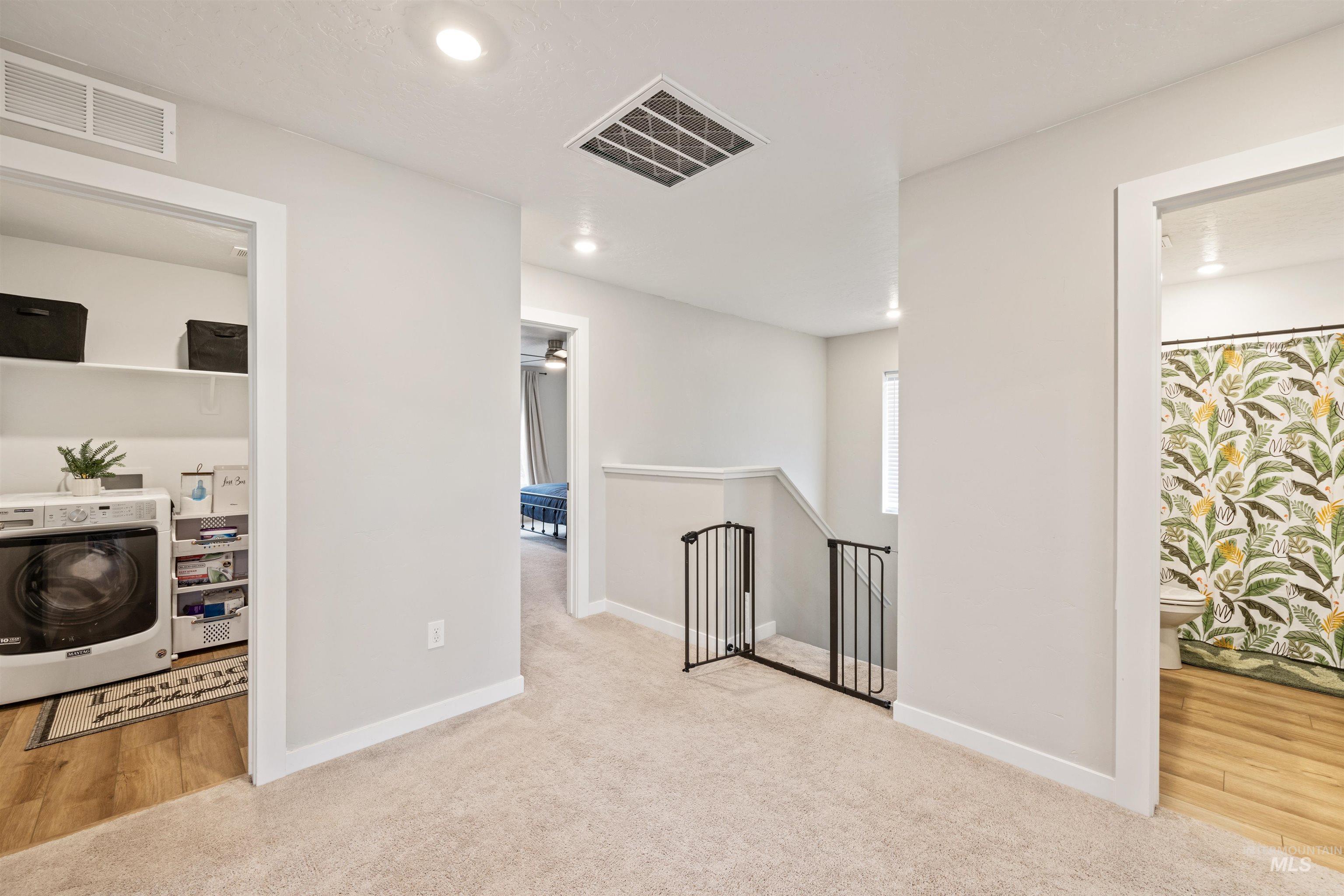 Hall featuring washer / clothes dryer, an upstairs landing, light carpet, recessed lighting, and light wood-type flooring