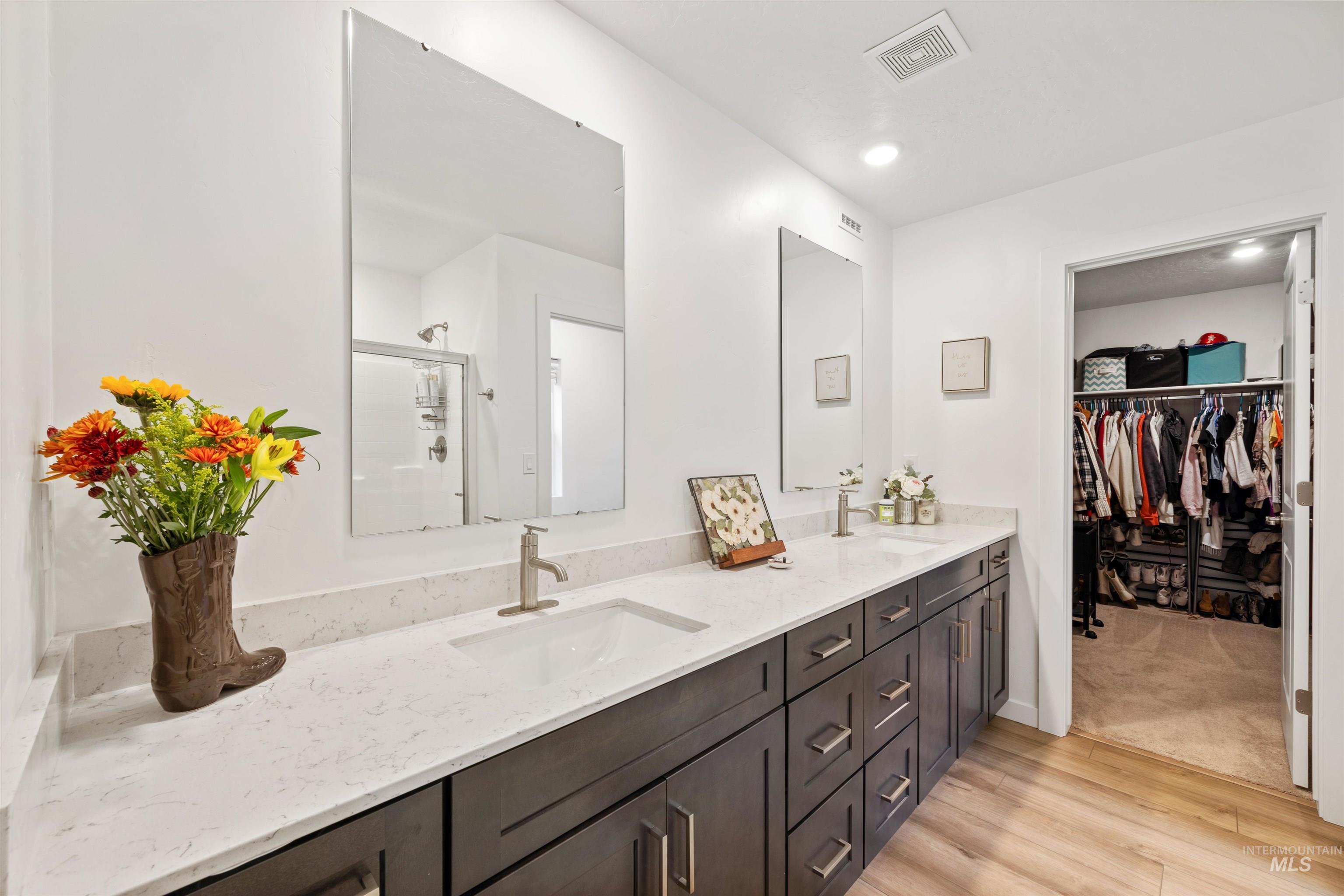 Full bathroom featuring light wood finished floors, double vanity, a stall shower, a walk in closet, and recessed lighting