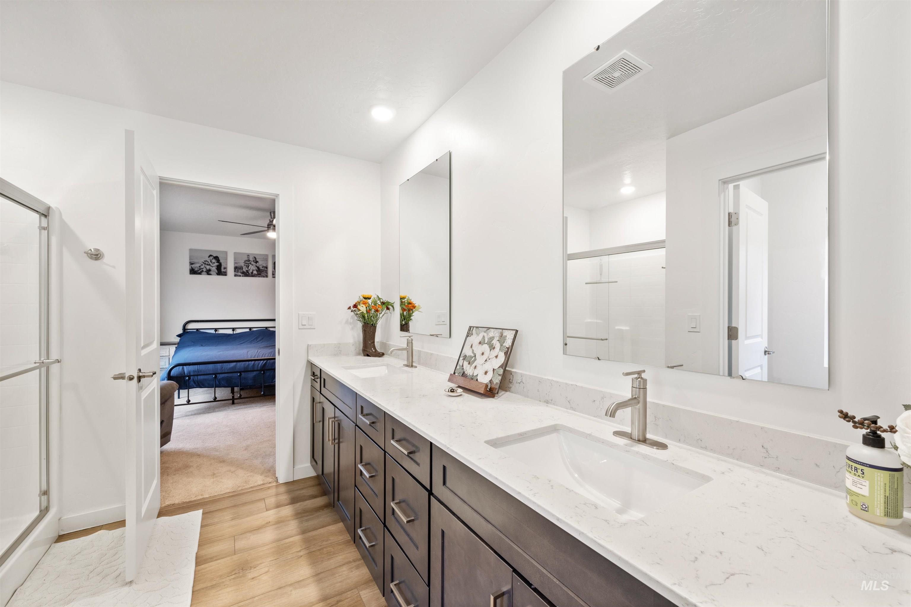 Full bath featuring double vanity, light wood finished floors, a shower stall, ensuite bathroom, and a ceiling fan