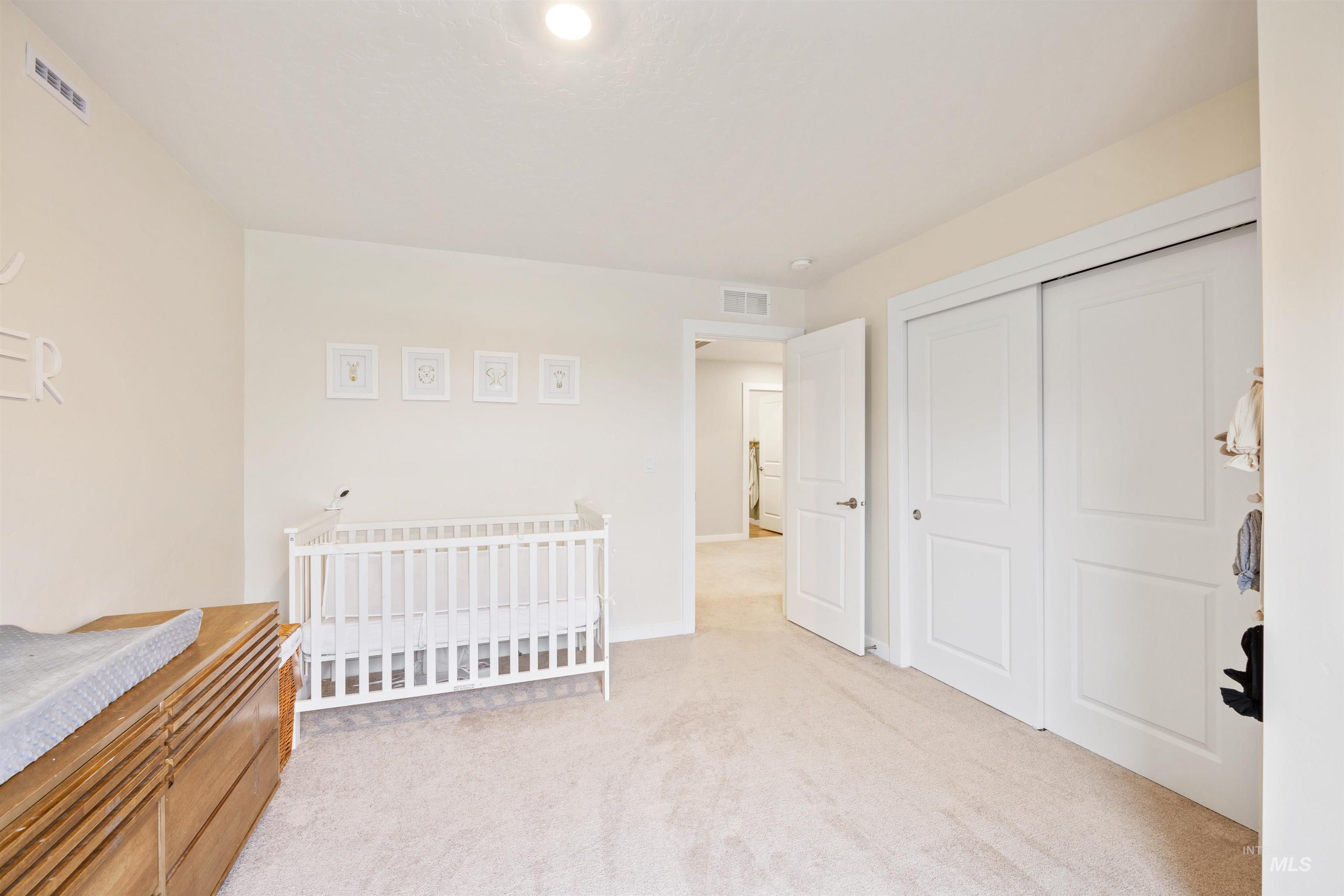Bedroom featuring light carpet, a crib, and a closet