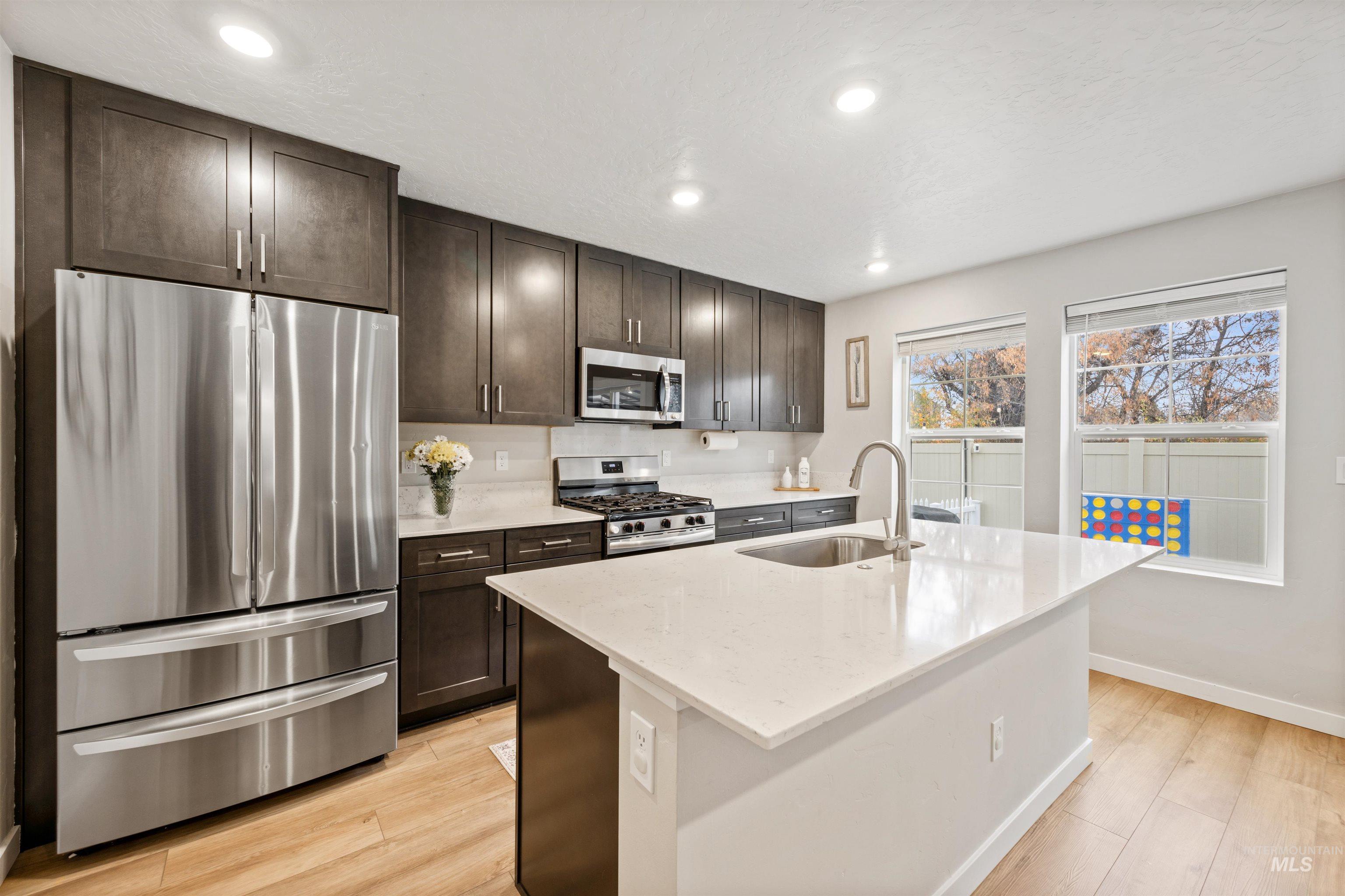 Kitchen with appliances with stainless steel finishes, light stone countertops, light wood-style floors, recessed lighting, and dark brown cabinetry