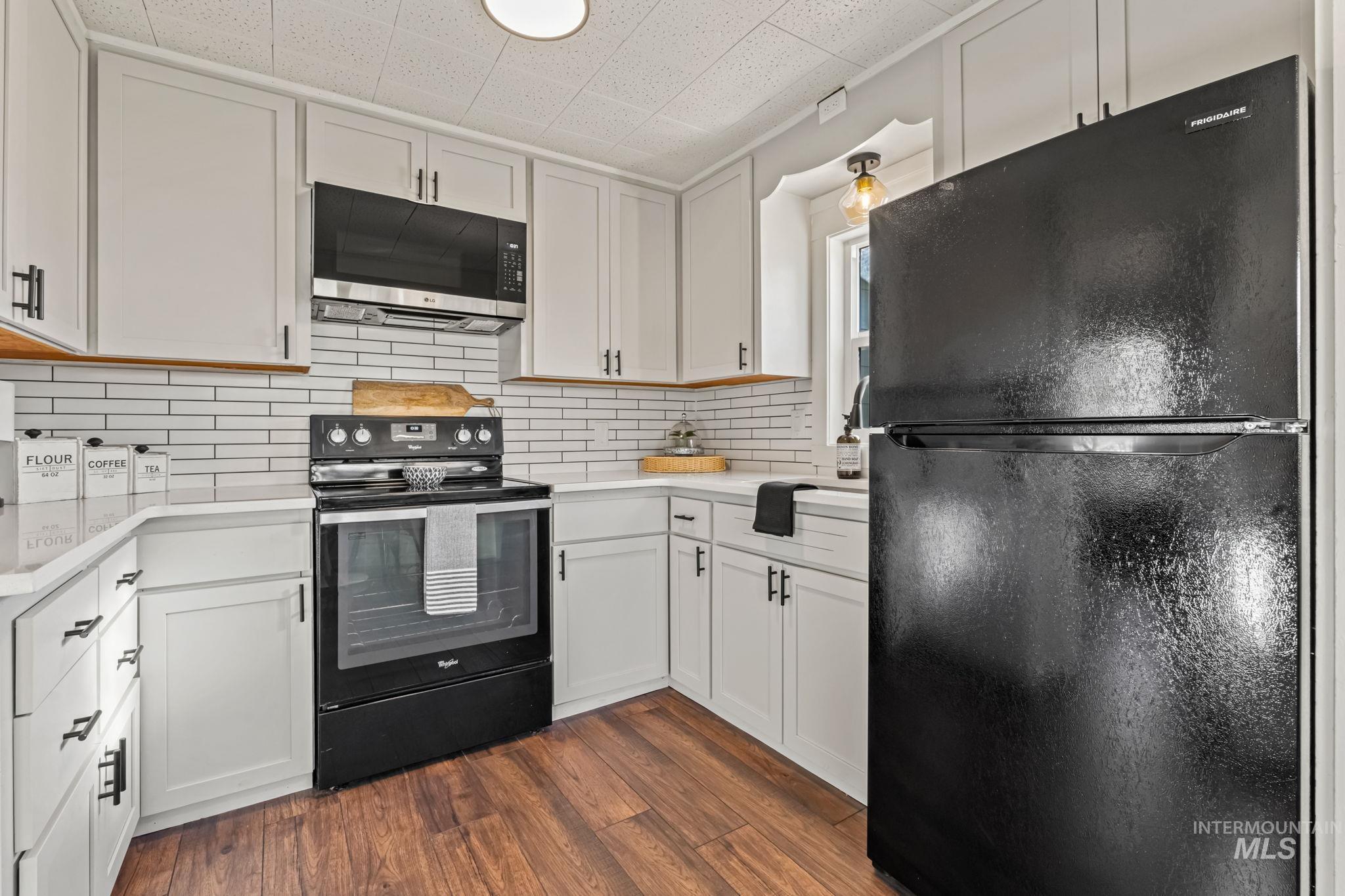 Kitchen with black appliances, white cabinets, dark wood-style floors, backsplash, and light stone counters