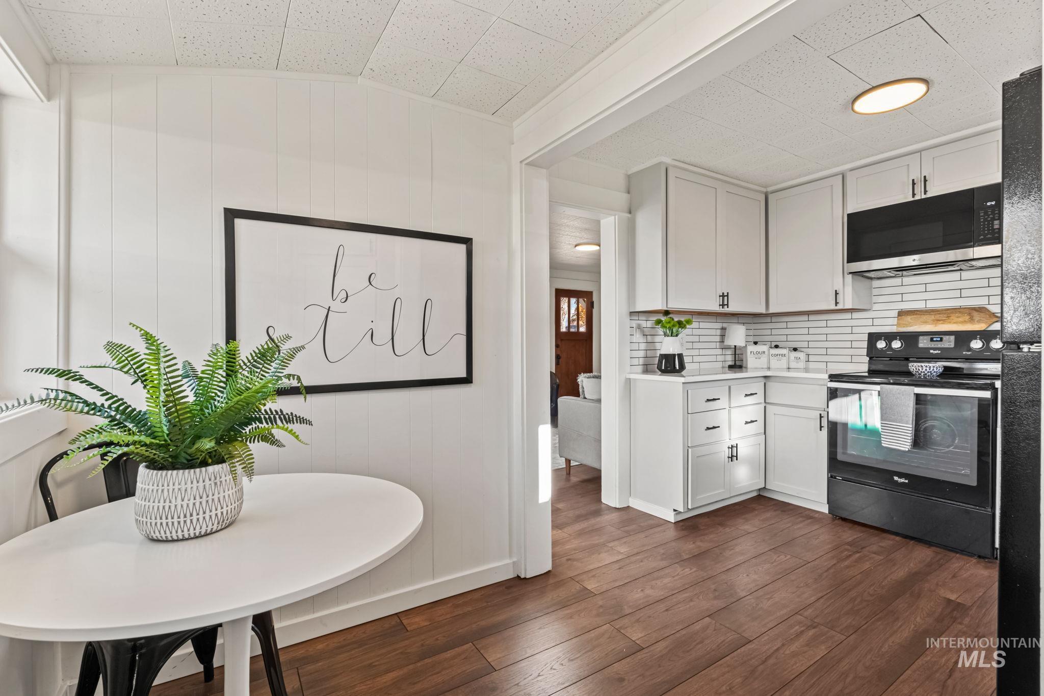 Kitchen with black appliances, white cabinetry, light countertops, dark wood-style floors, and decorative backsplash