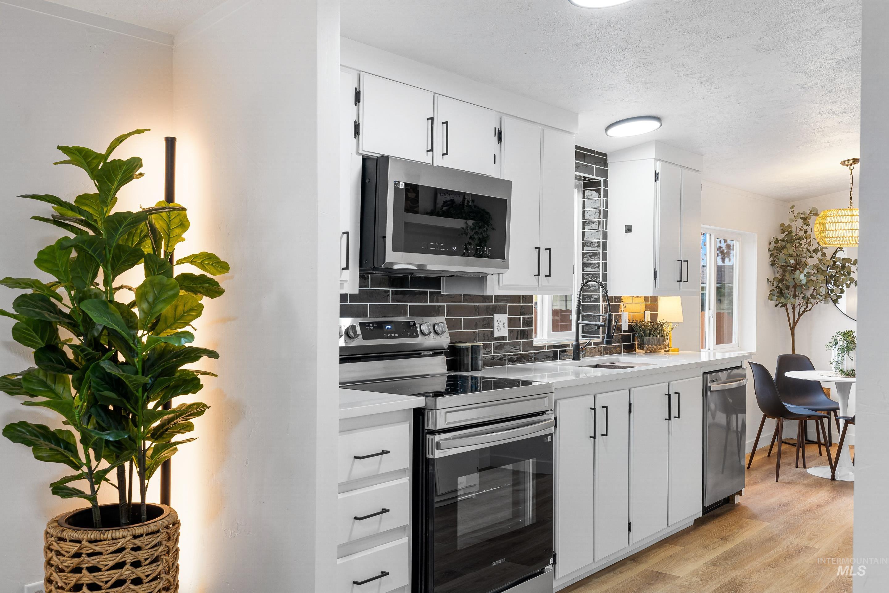 Kitchen with appliances with stainless steel finishes, tasteful backsplash, white cabinetry, light wood-style floors, and a textured ceiling