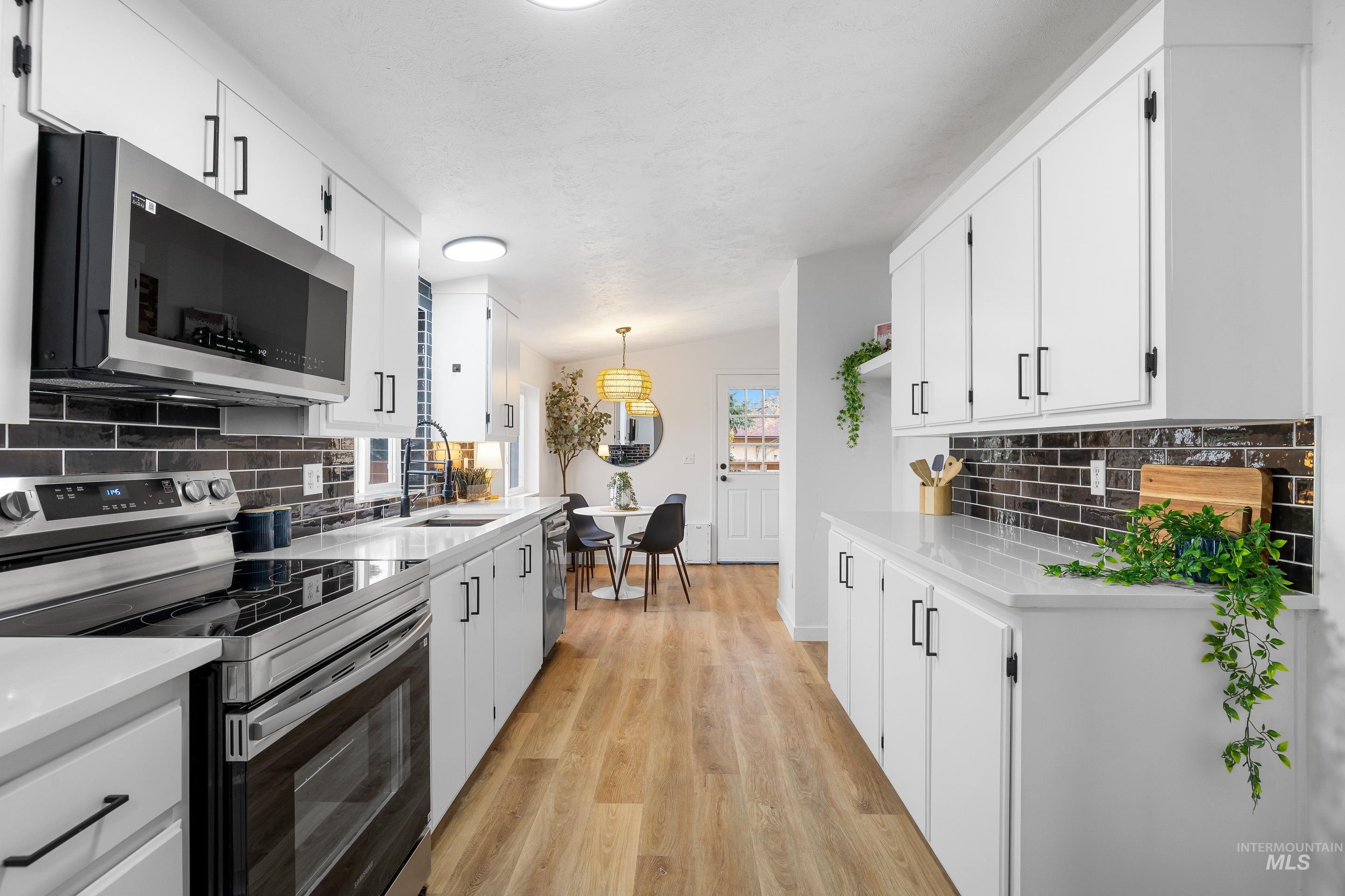 Kitchen featuring backsplash, appliances with stainless steel finishes, light wood-style flooring, and light stone countertops
