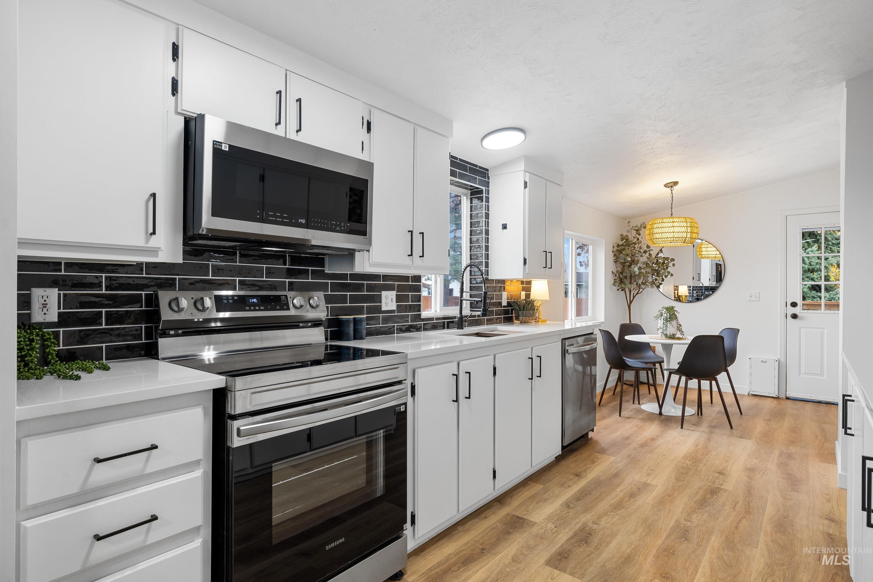 Kitchen with stainless steel appliances, decorative backsplash, white cabinets, light wood-style floors, and healthy amount of natural light