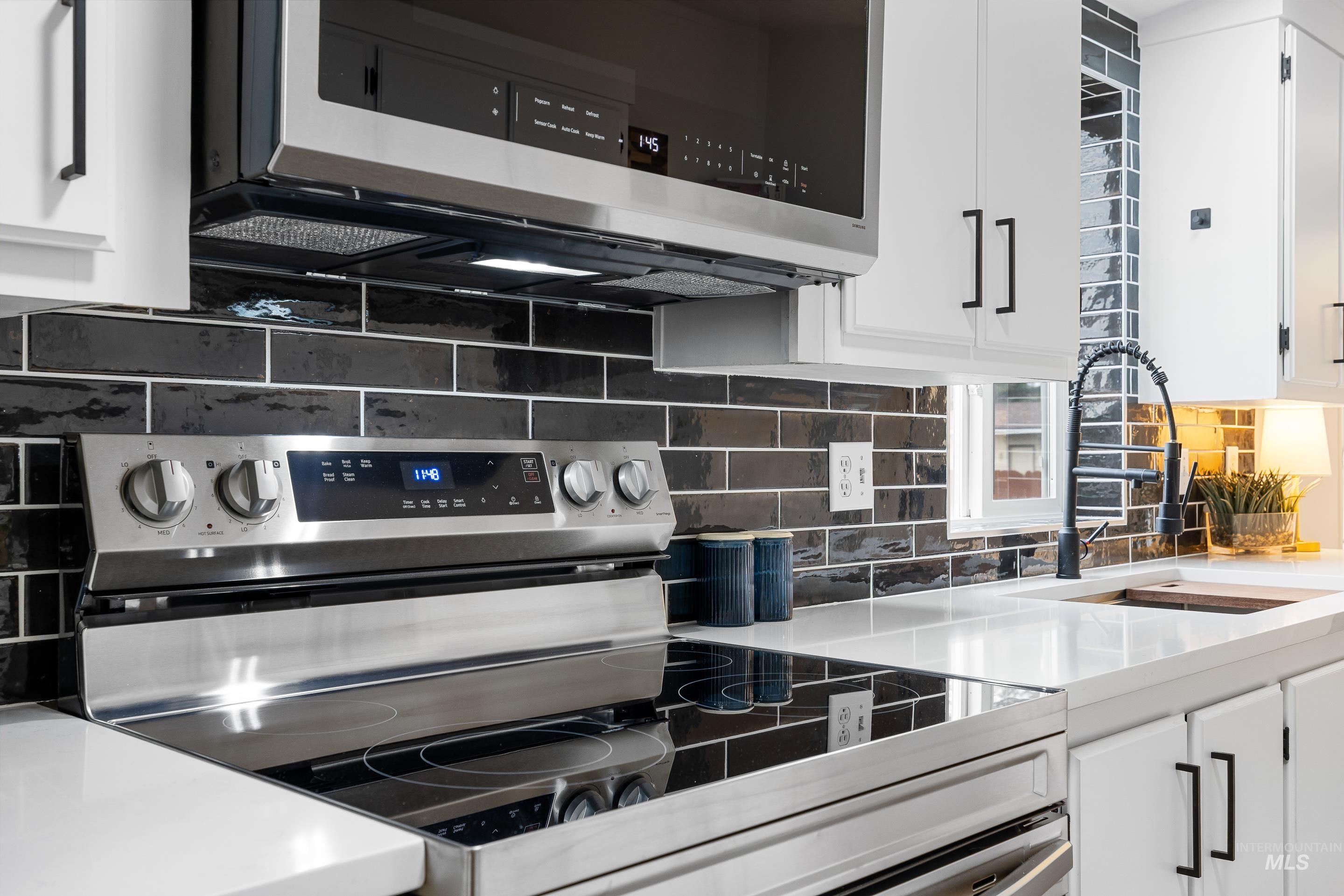 Kitchen featuring stainless steel appliances, tasteful backsplash, white cabinetry, and light stone countertops