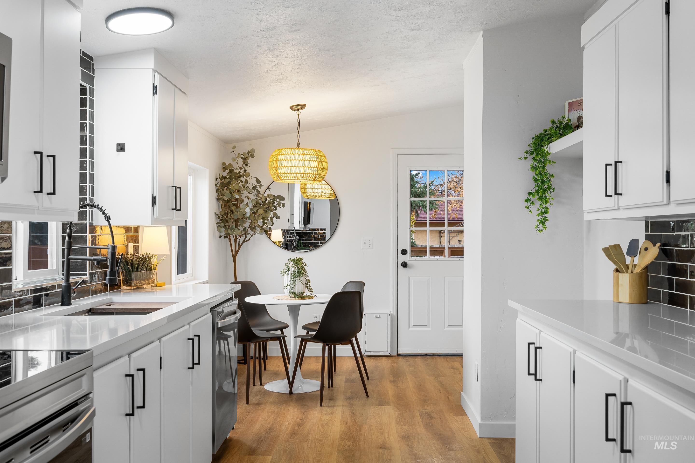 Kitchen featuring decorative backsplash, white cabinets, light wood-type flooring, hanging light fixtures, and vaulted ceiling