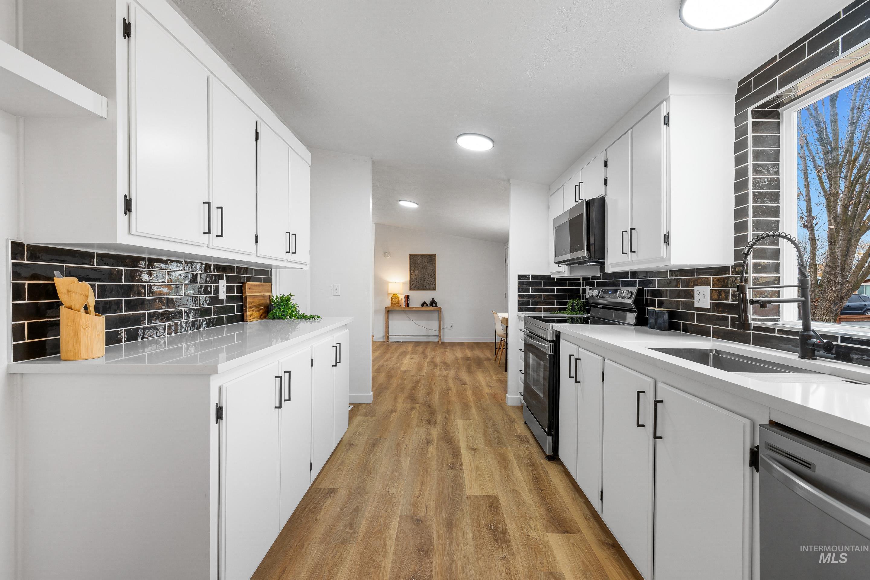 Kitchen with backsplash, appliances with stainless steel finishes, light stone countertops, and white cabinets