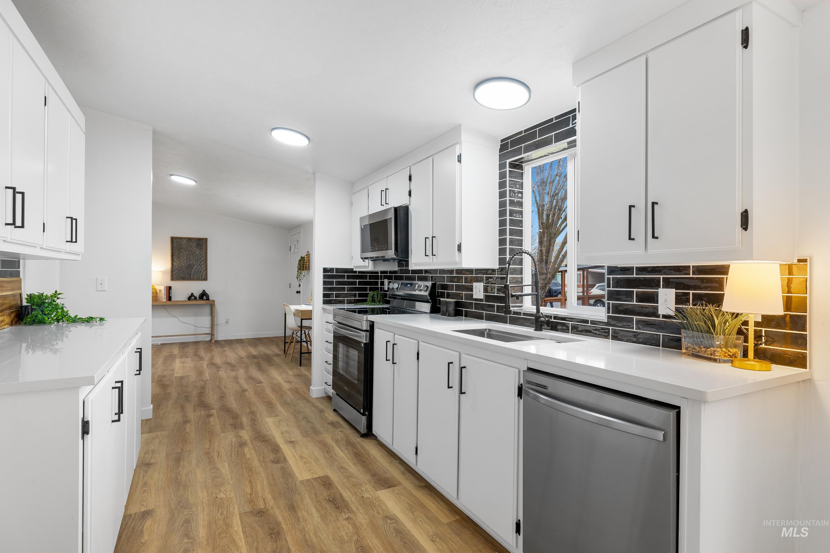 Kitchen with tasteful backsplash, stainless steel appliances, white cabinetry, light wood finished floors, and light stone countertops