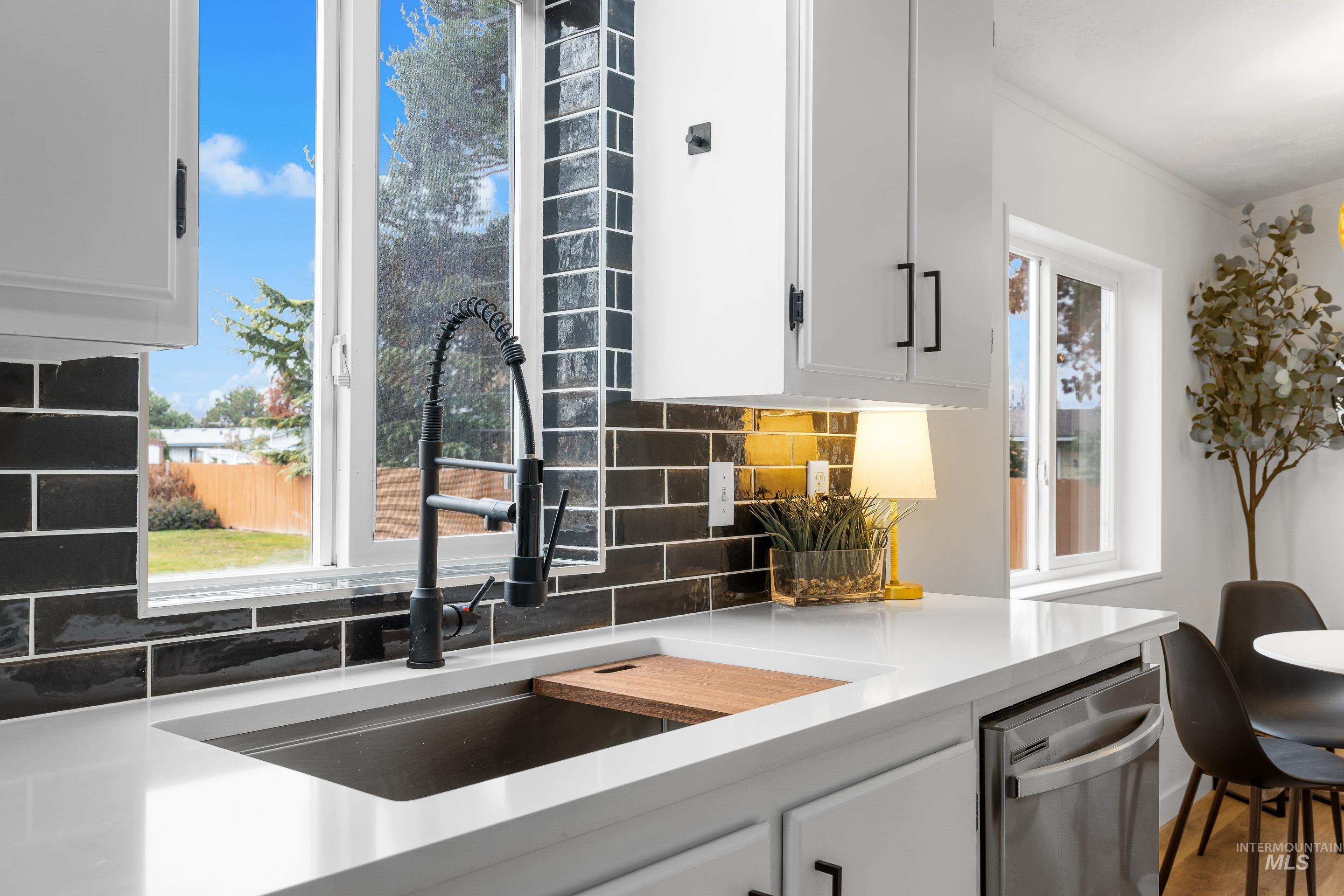 Kitchen featuring white cabinets, backsplash, light stone counters, and stainless steel dishwasher