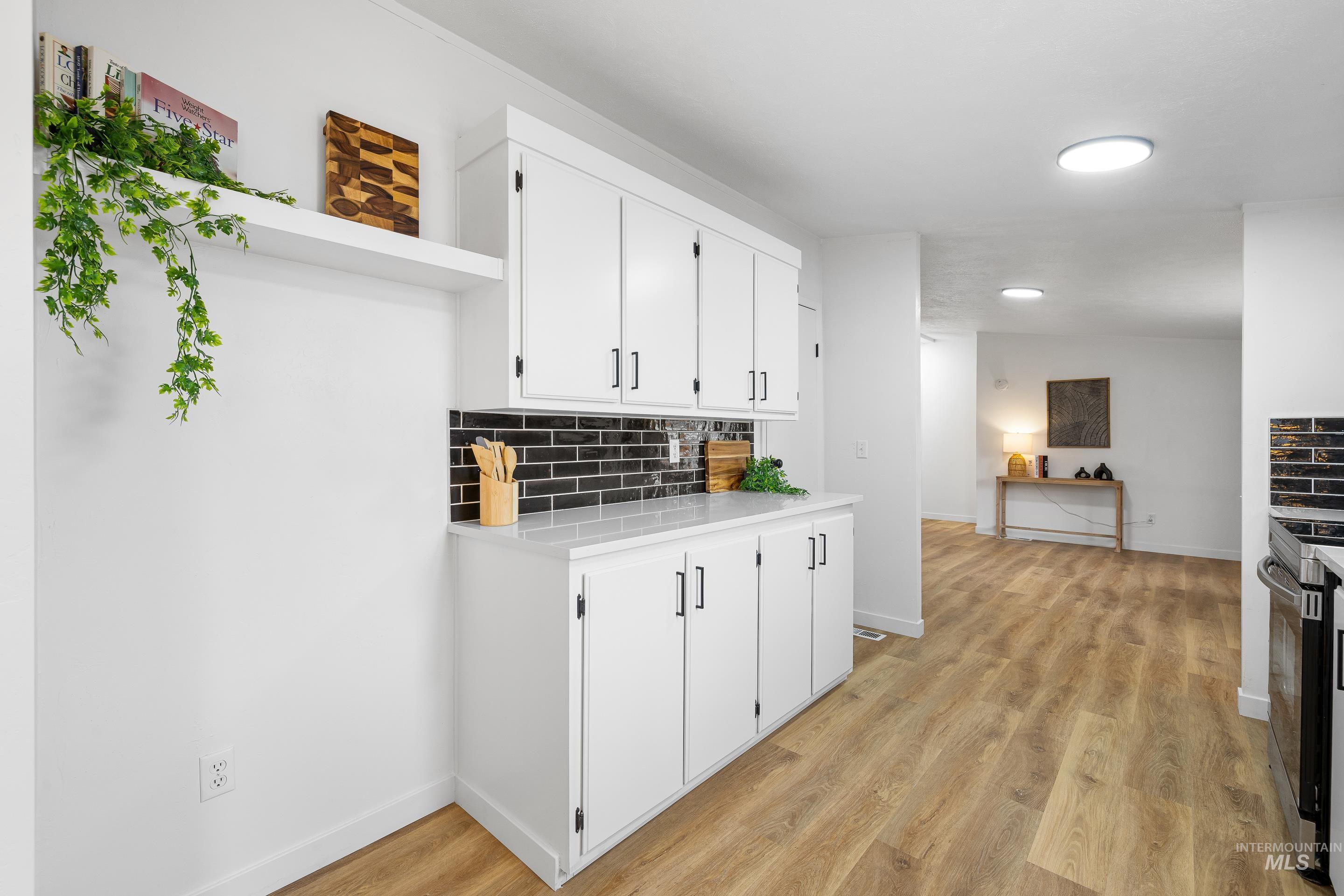 Kitchen with backsplash, light wood finished floors, white cabinets, open shelves, and stainless steel range with electric stovetop
