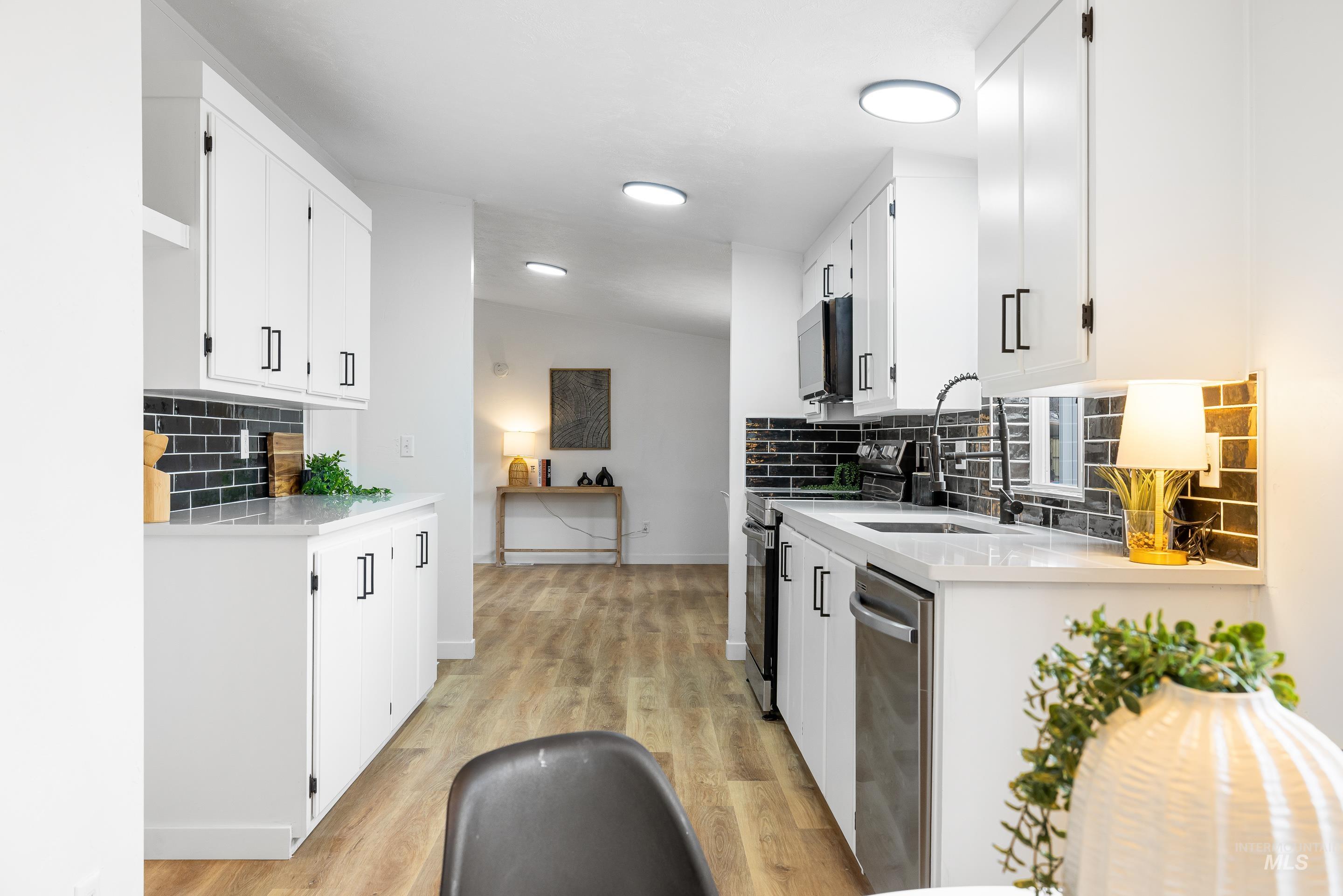 Kitchen with decorative backsplash, light stone countertops, white cabinets, appliances with stainless steel finishes, and vaulted ceiling