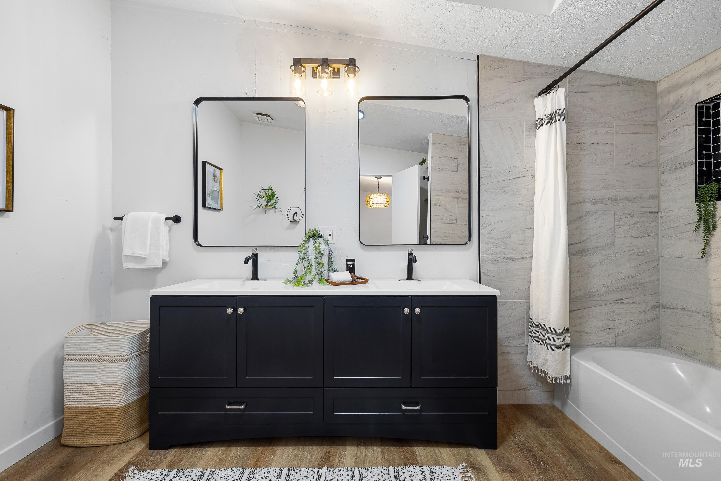 Full bathroom with double vanity, light wood-type flooring, and shower / tub combo with curtain