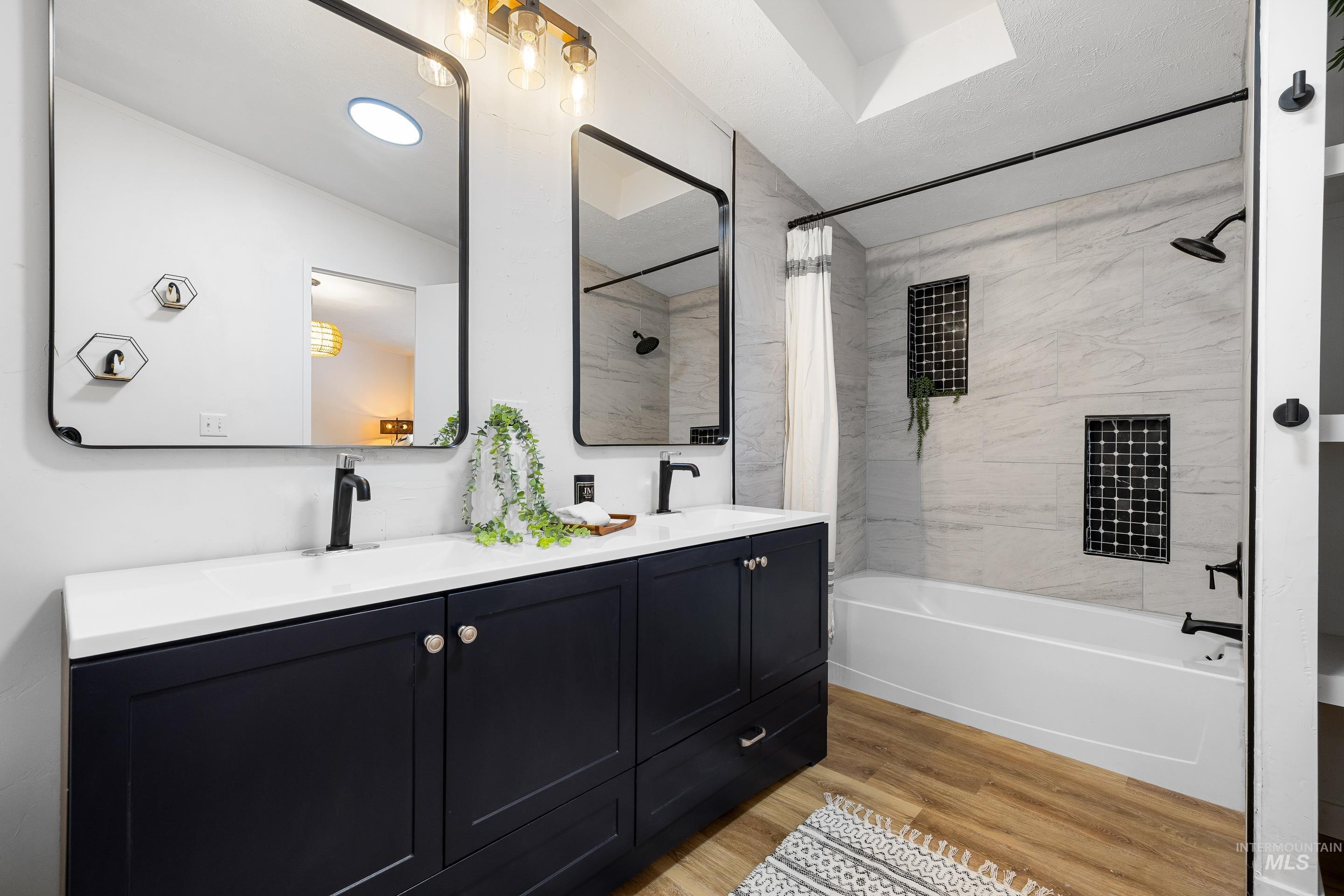 Full bath featuring shower / bathtub combination with curtain, light wood-style flooring, and double vanity