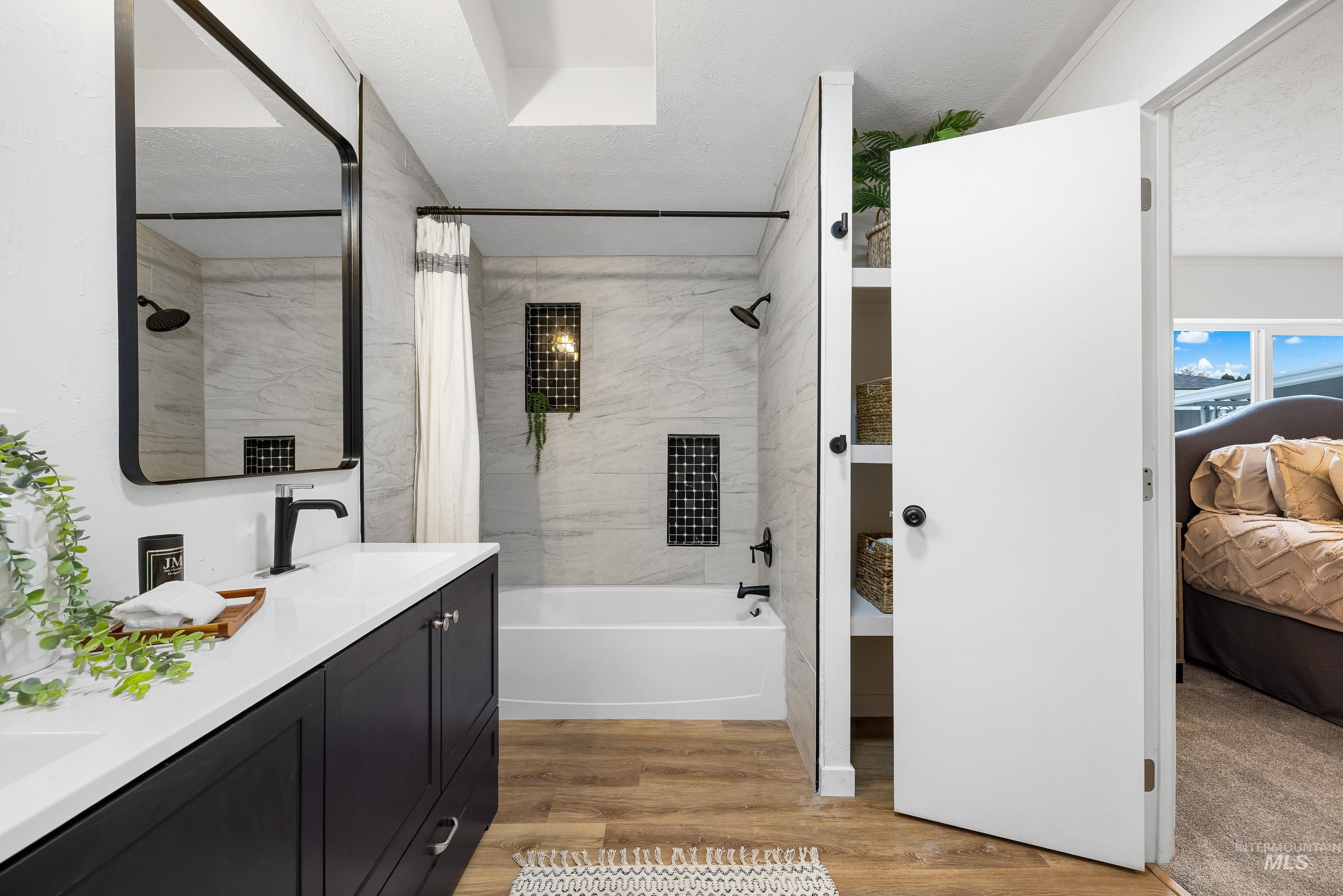 Bathroom with shower / bathtub combination with curtain, light wood-style floors, ensuite bathroom, double vanity, and a textured ceiling
