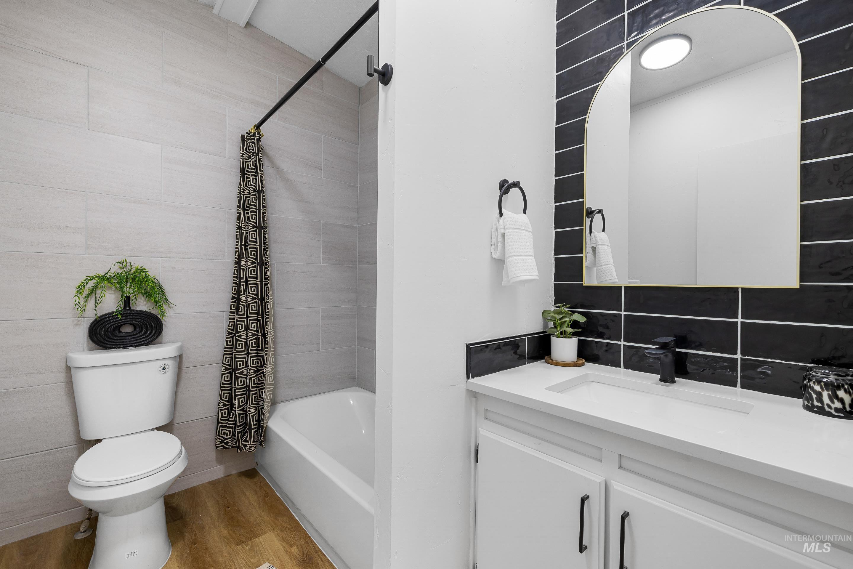 Bathroom featuring light wood-type flooring, vanity, shower / bath combination with curtain, and backsplash