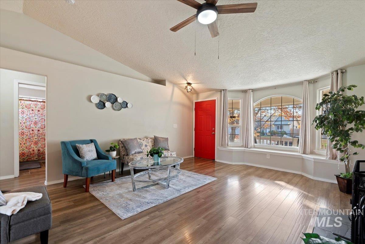 Living area with a textured ceiling, lofted ceiling, wood finished floors, and ceiling fan