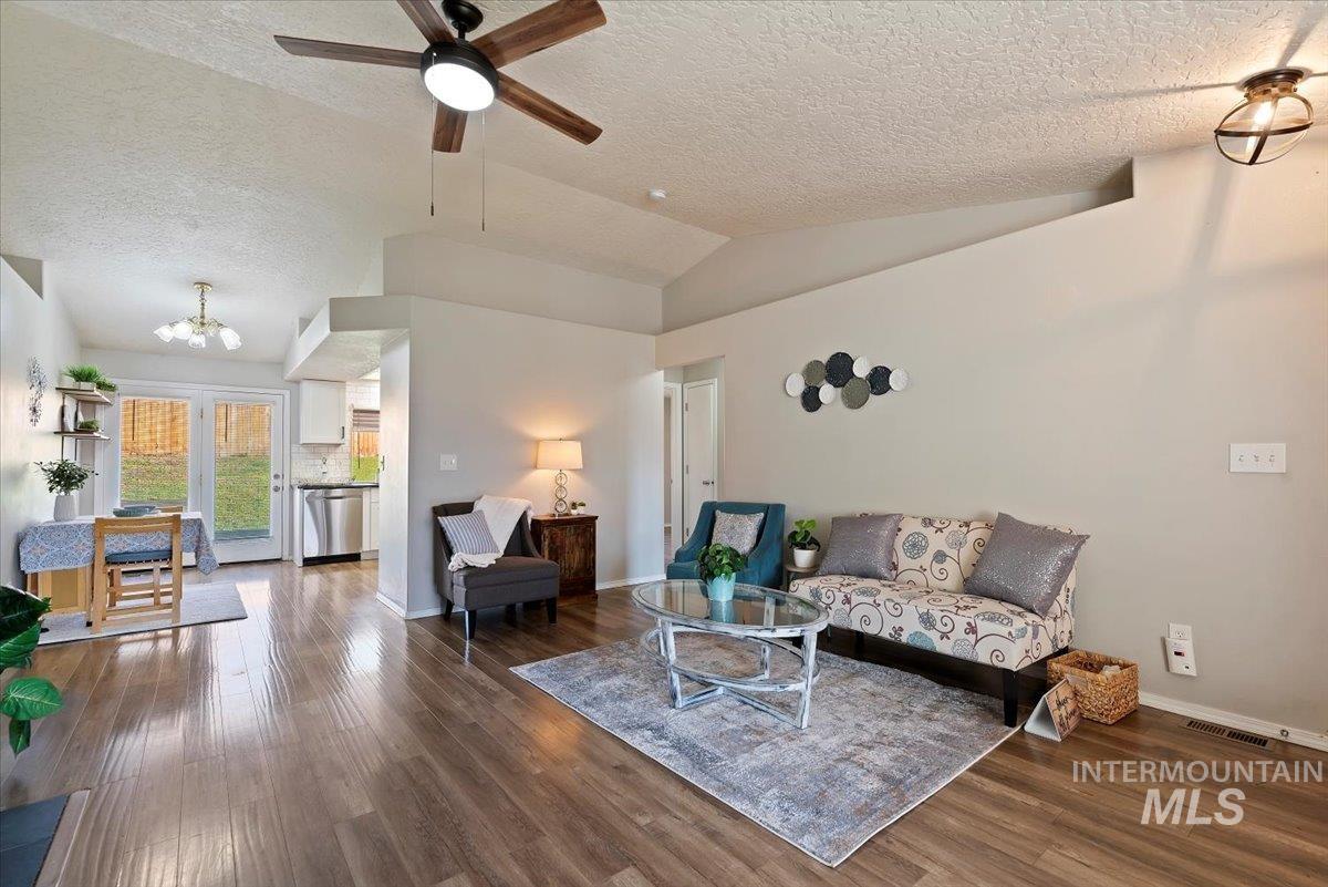 Living room featuring lofted ceiling, wood finished floors, a textured ceiling, a chandelier, and ceiling fan