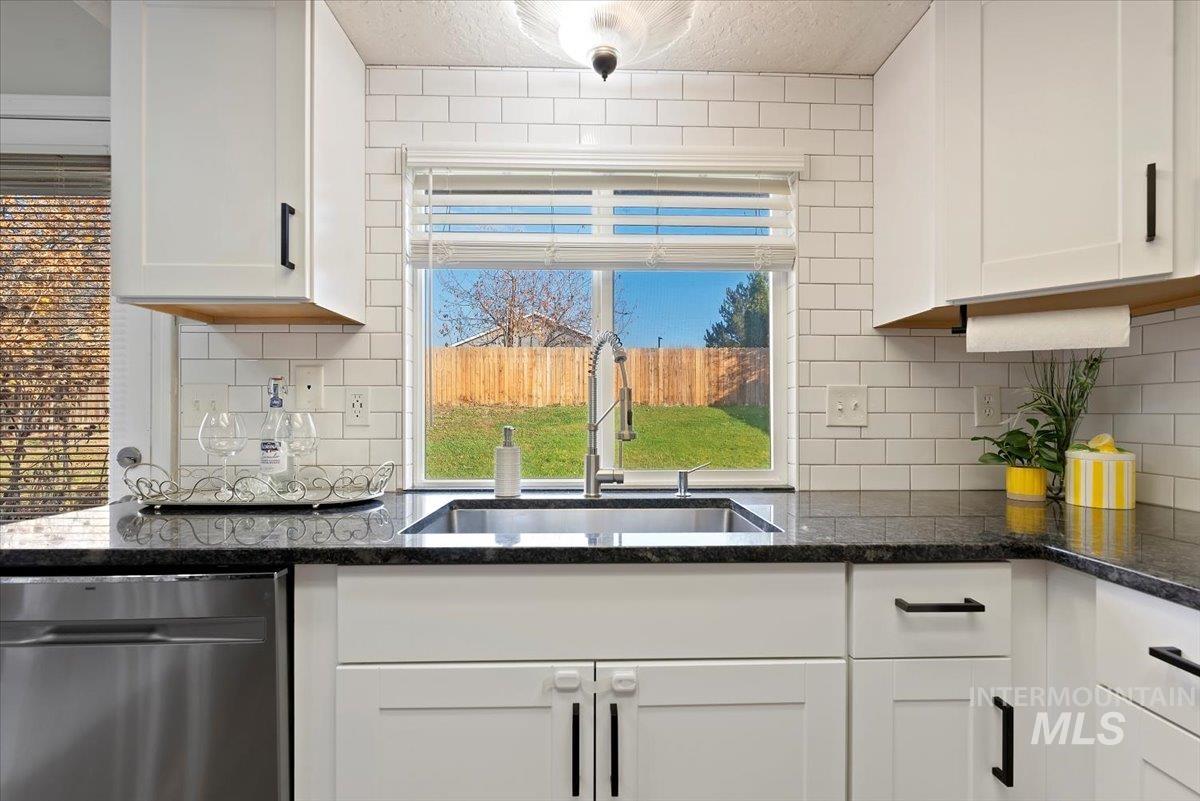 Kitchen featuring stainless steel dishwasher, white cabinetry, tasteful backsplash, and a textured ceiling