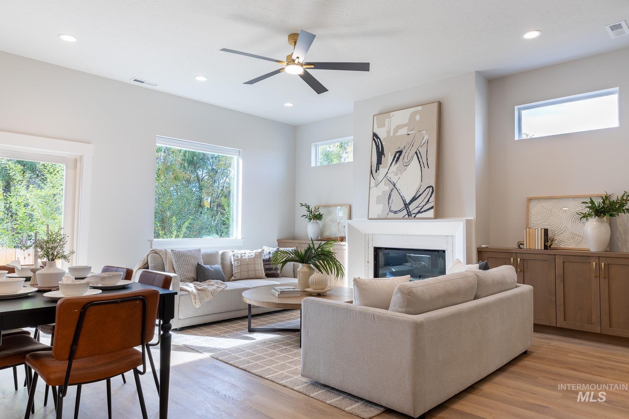 Living area with healthy amount of natural light, light wood finished floors, a glass covered fireplace, ceiling fan, and recessed lighting