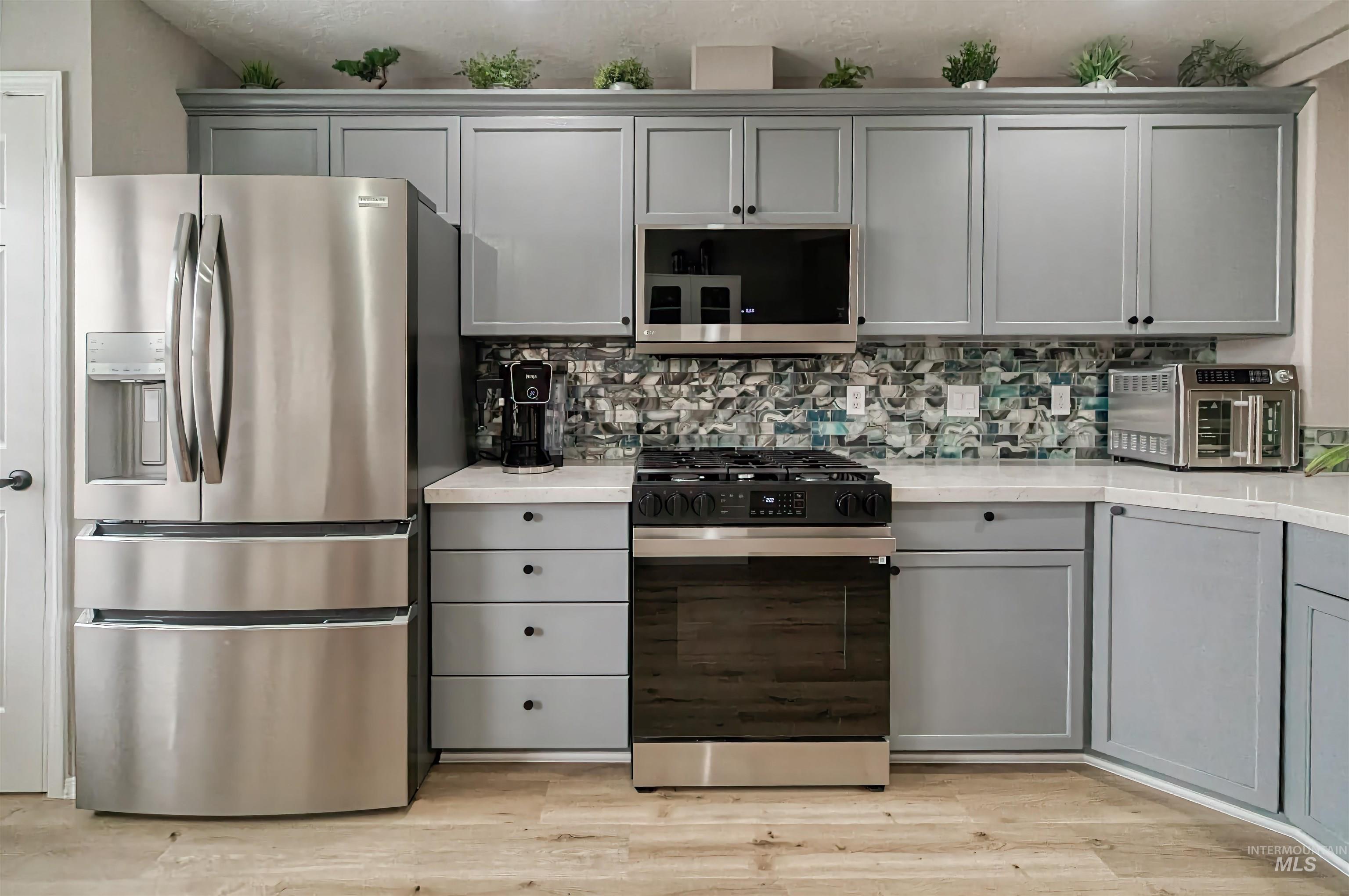 Kitchen featuring gray cabinetry, appliances with stainless steel finishes, decorative backsplash, and light wood-type flooring