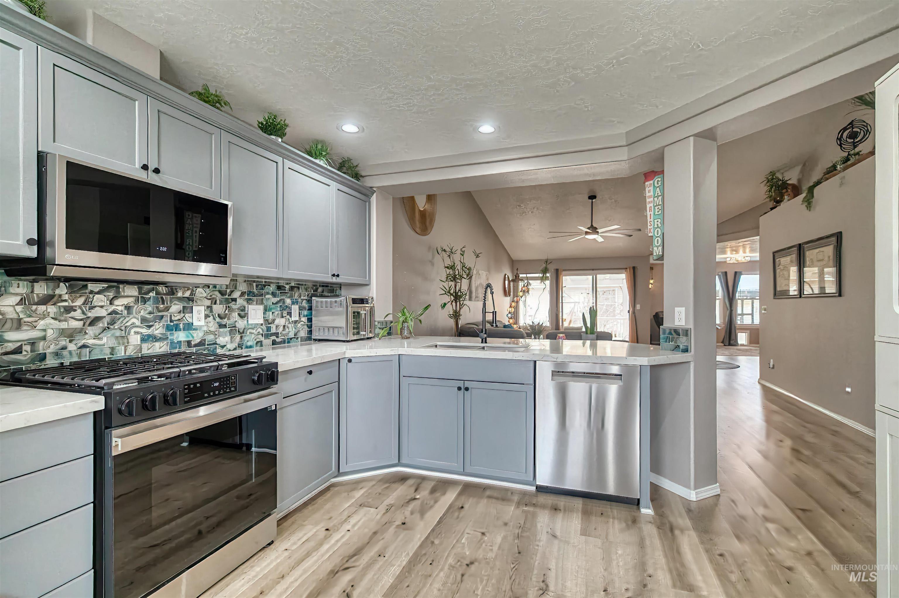 Kitchen with gray cabinetry, appliances with stainless steel finishes, backsplash, open floor plan, and a textured ceiling