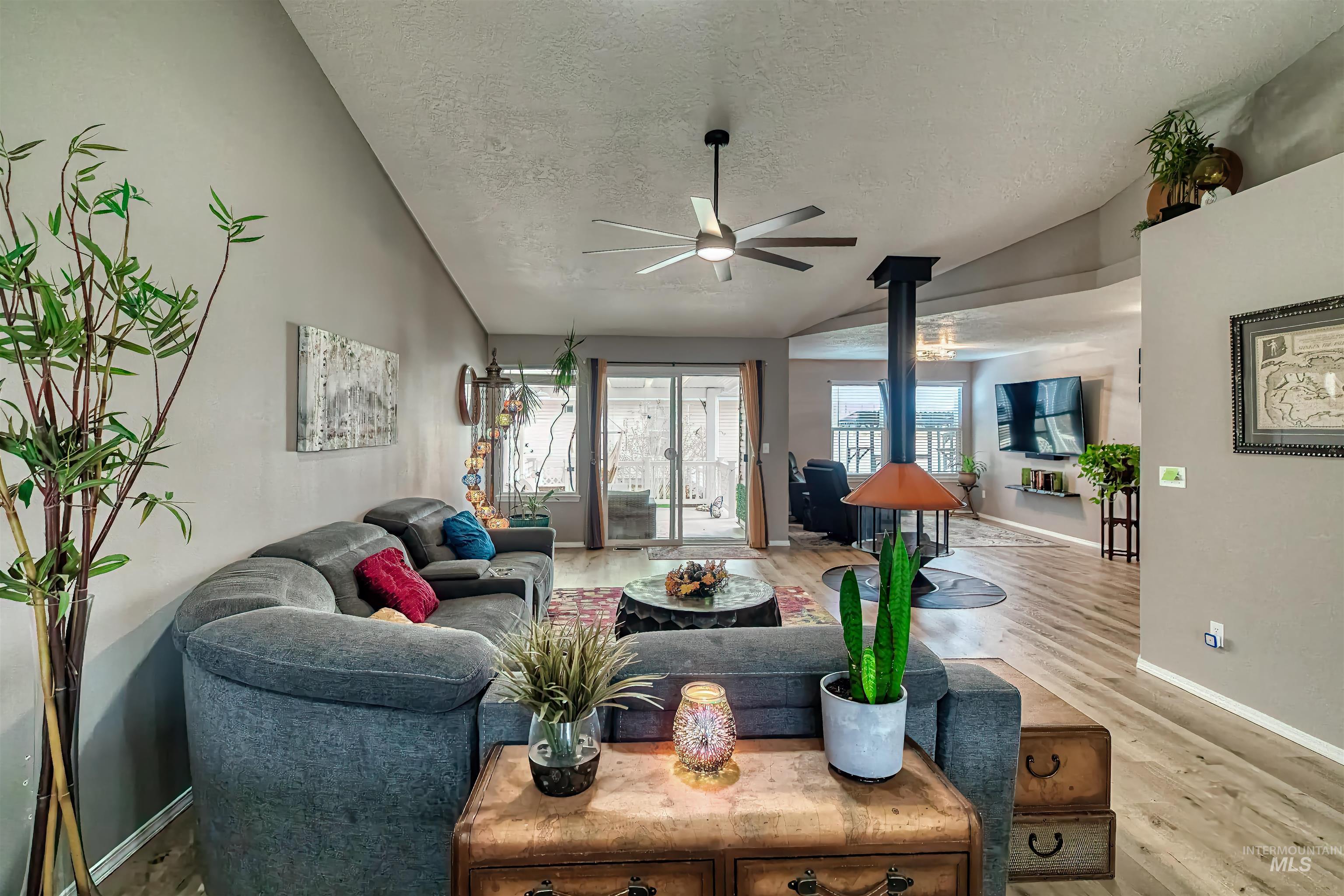 Living area with a wood stove, vaulted ceiling, light wood finished floors, a textured ceiling, and ceiling fan