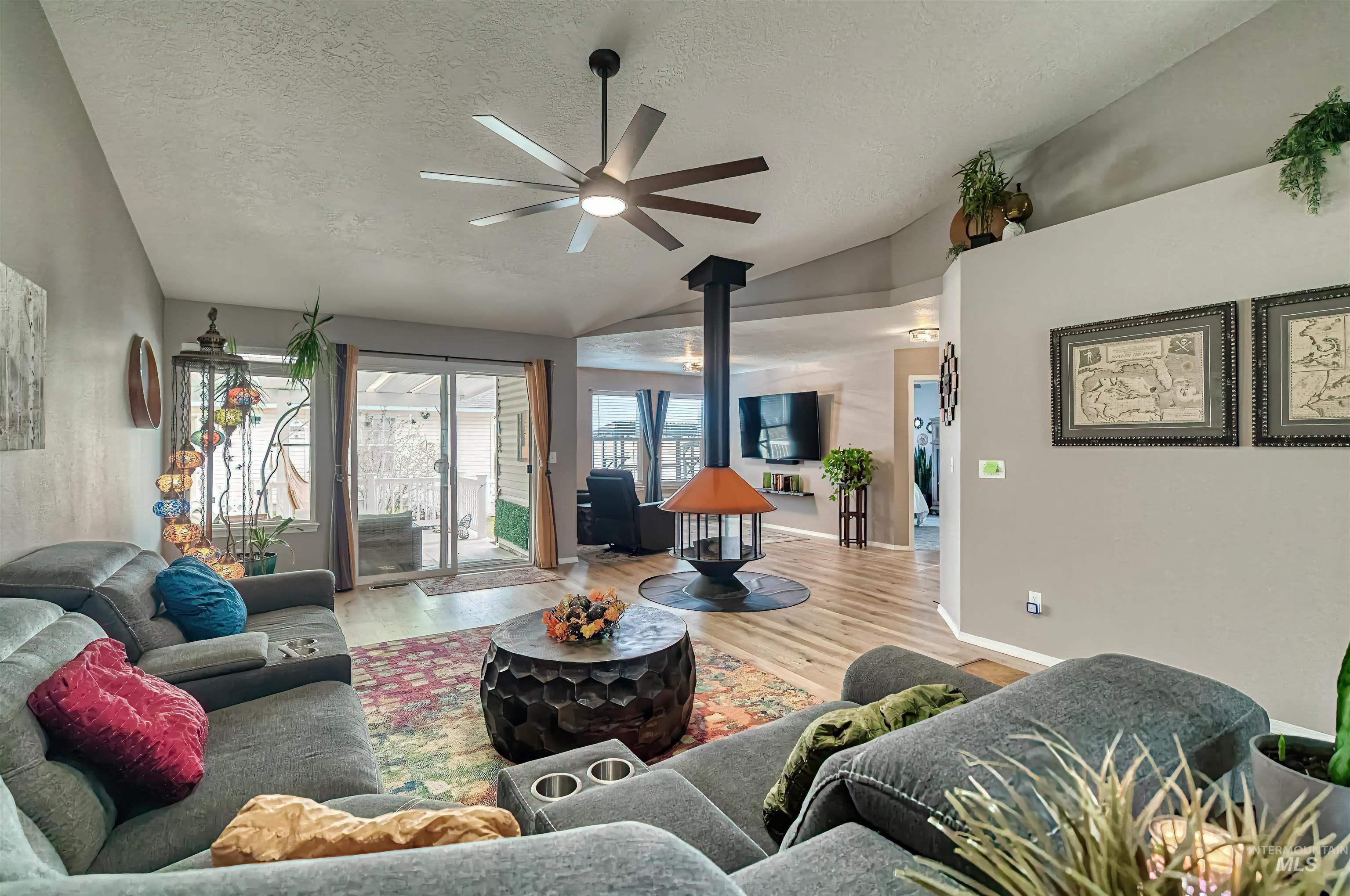Living area with a wood stove, a textured ceiling, wood finished floors, vaulted ceiling, and ceiling fan