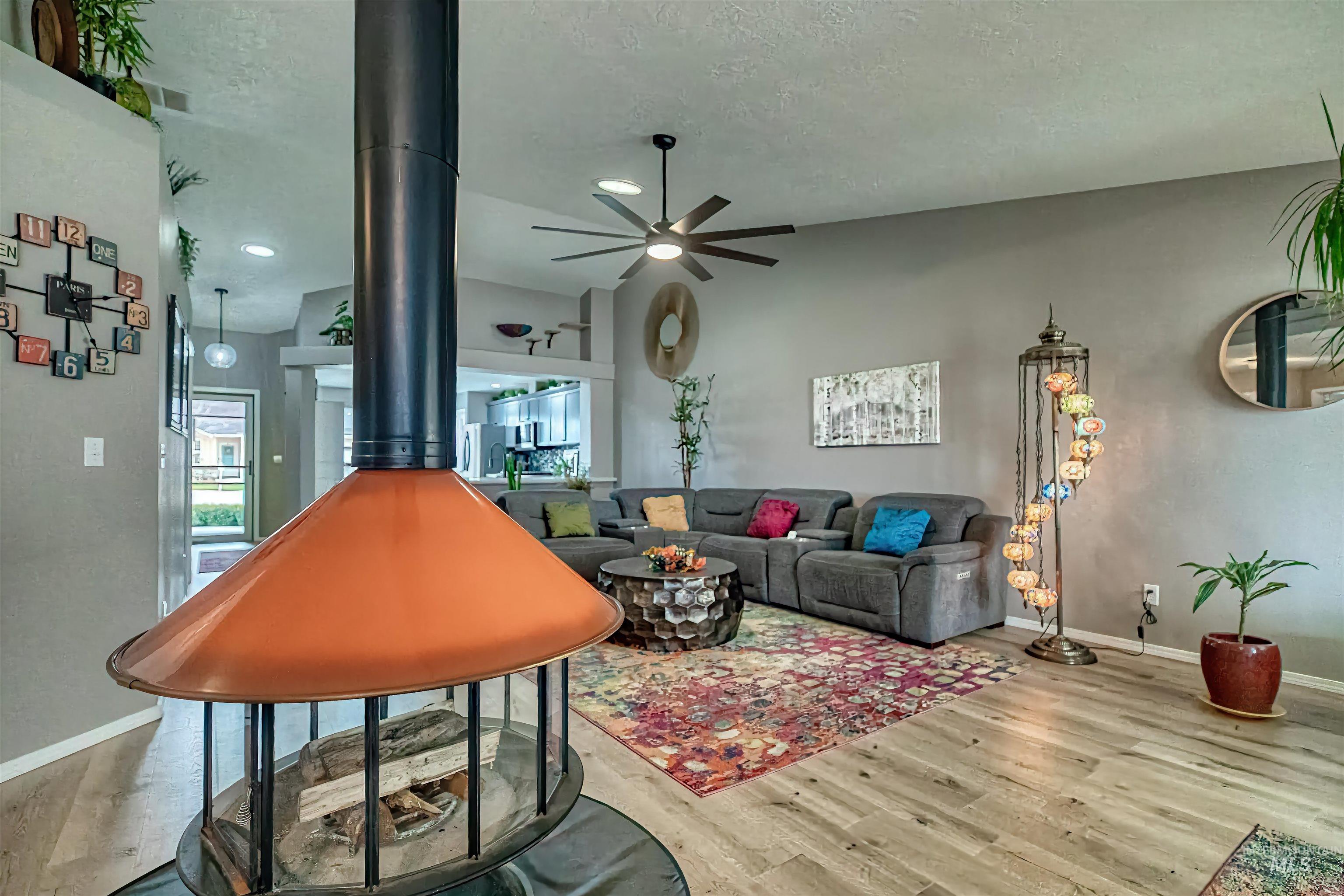 Living room with vaulted ceiling, wood finished floors, ceiling fan, a textured ceiling, and a wood stove
