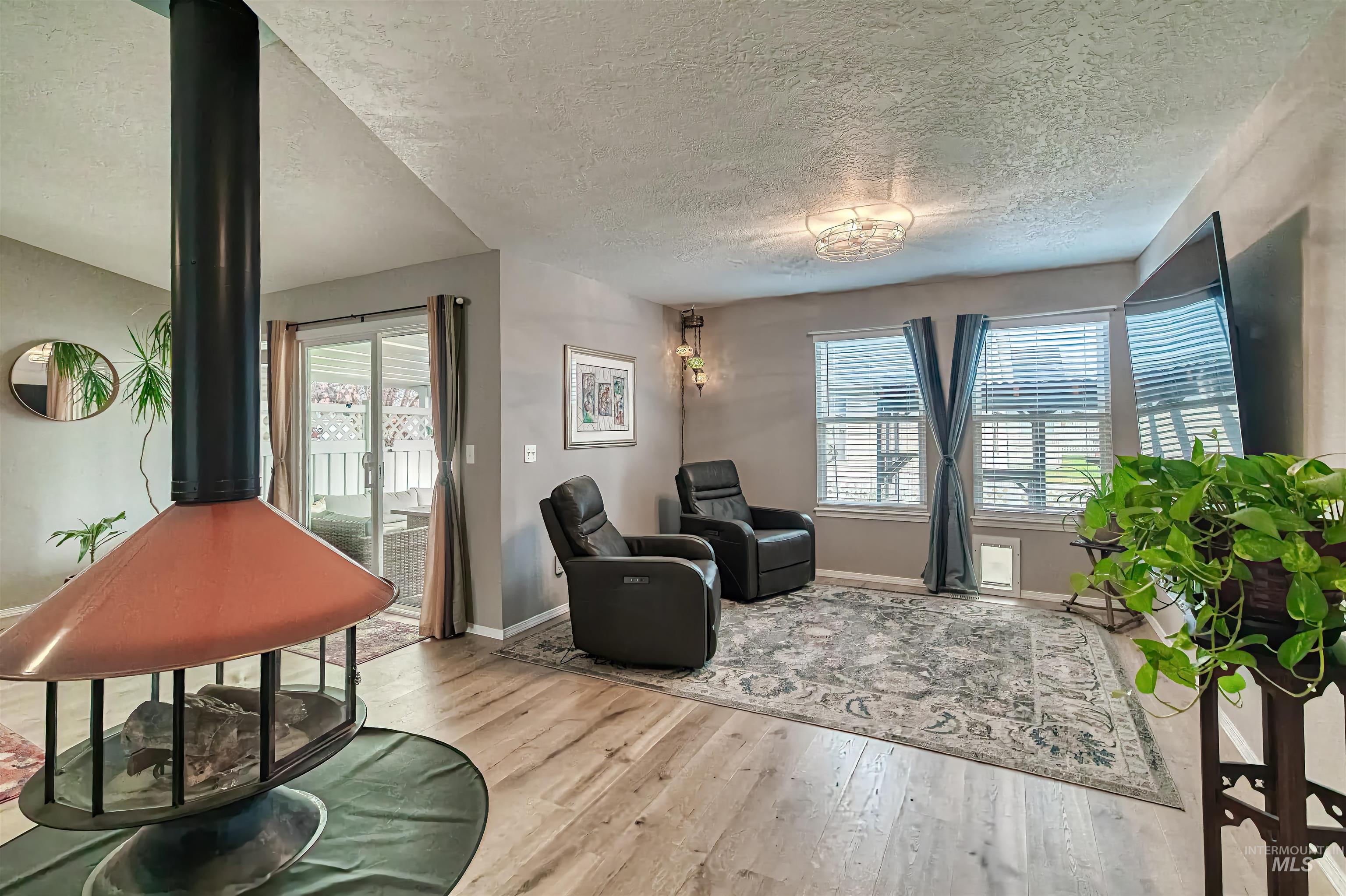 Living area with a textured ceiling, plenty of natural light, a wood stove, and light wood-style flooring