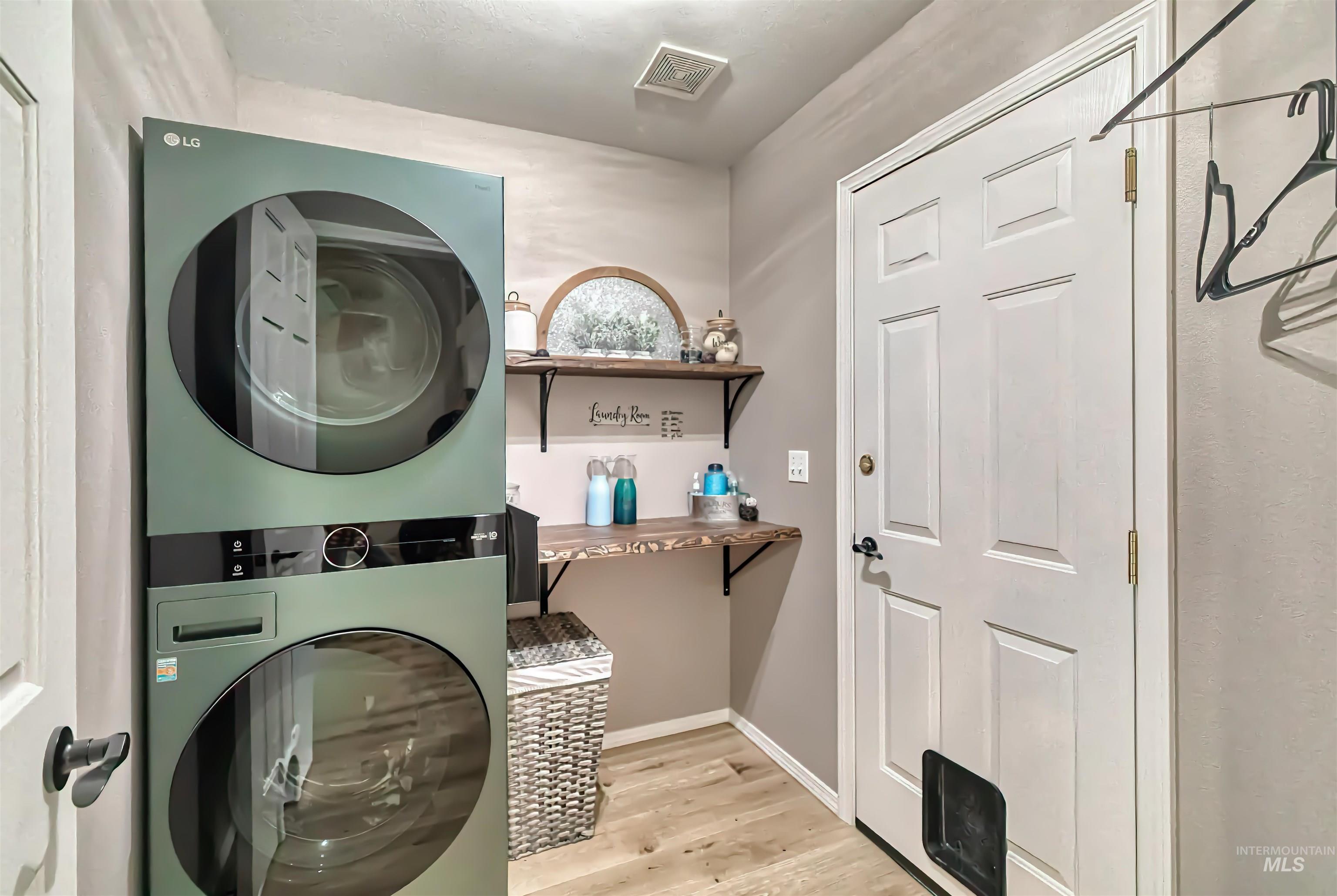 Washroom with light wood-style flooring and stacked washer and clothes dryer