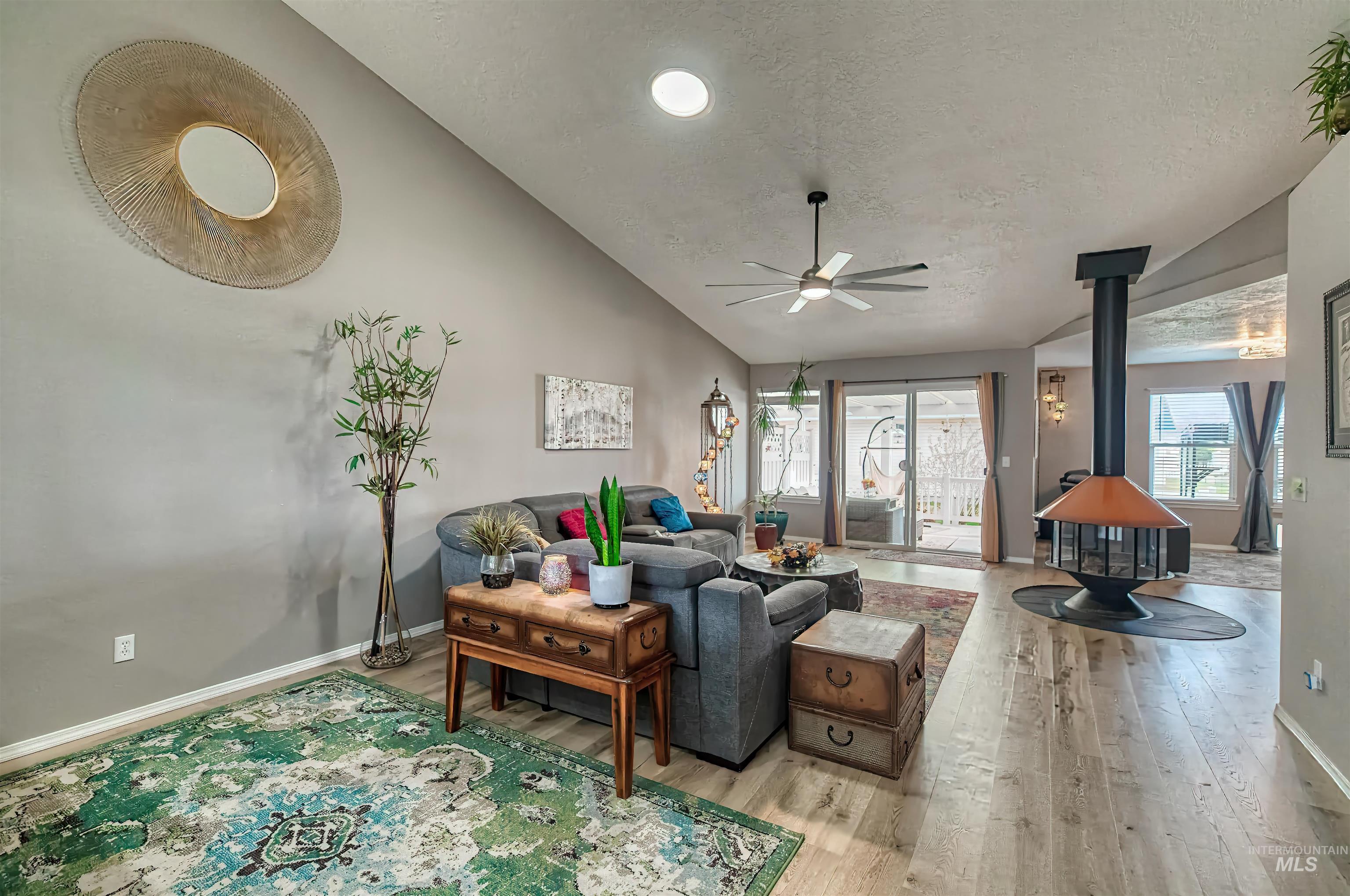 Living area with a wood stove, vaulted ceiling, light wood-style flooring, a textured ceiling, and ceiling fan